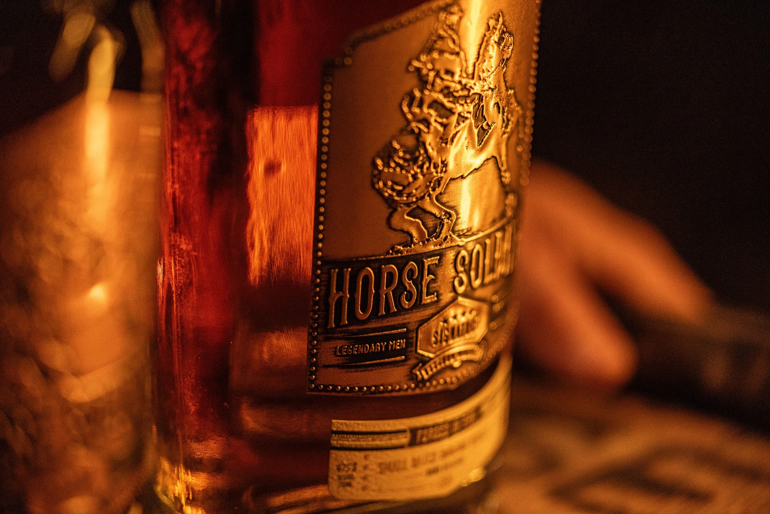 Close-up of a Crown Royal Horse Solider bottle label illuminated by warm light, featuring a horse and soldier emblem.