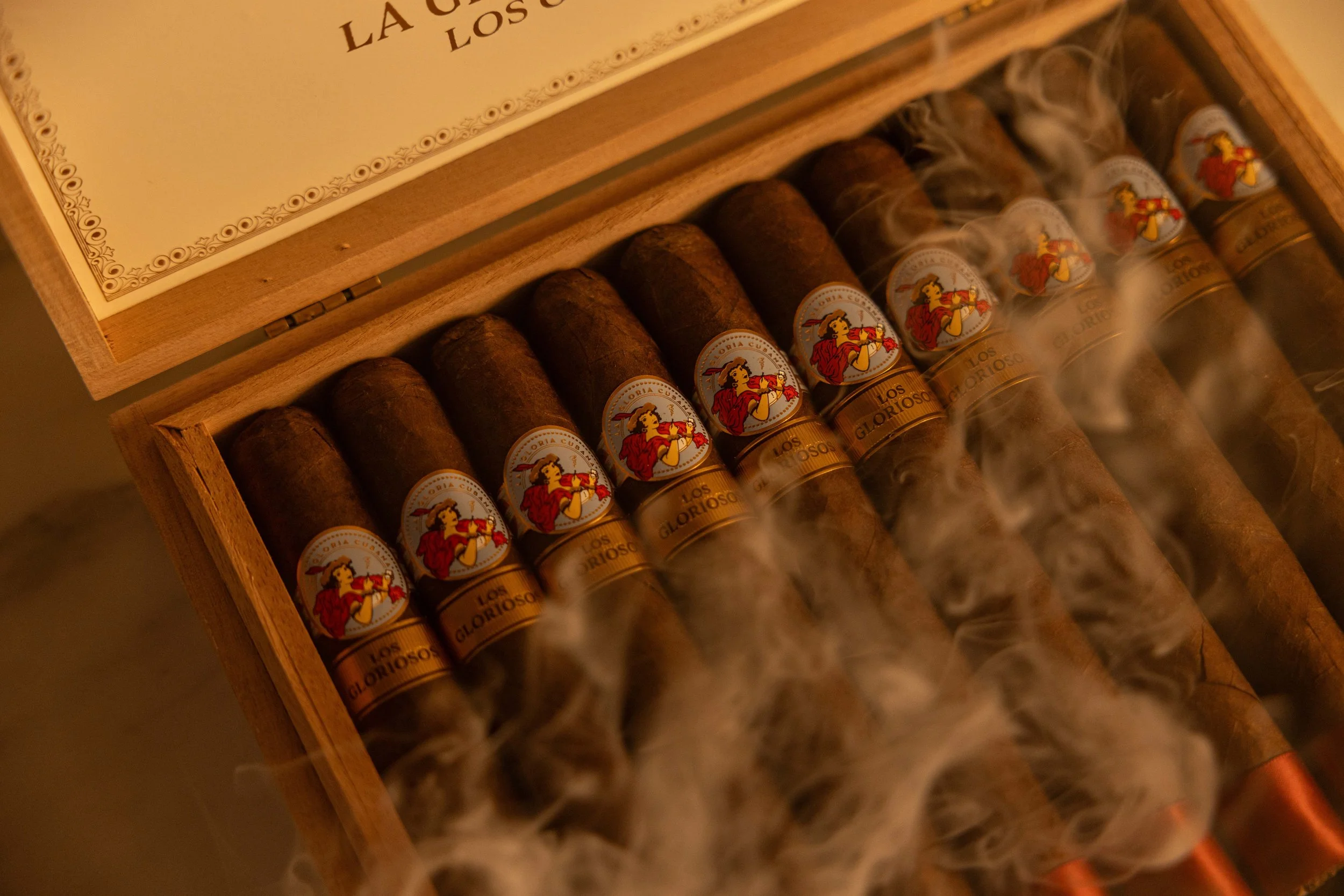 A box of cigars with colorful labels featuring a woman playing a violin. The cigars are emitting smoke.