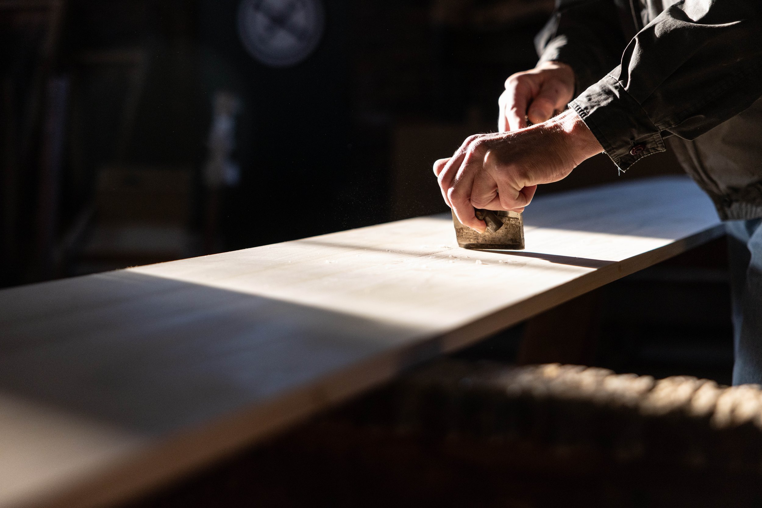 A person using a hand plane on a wooden workbench in a woodworking shop.