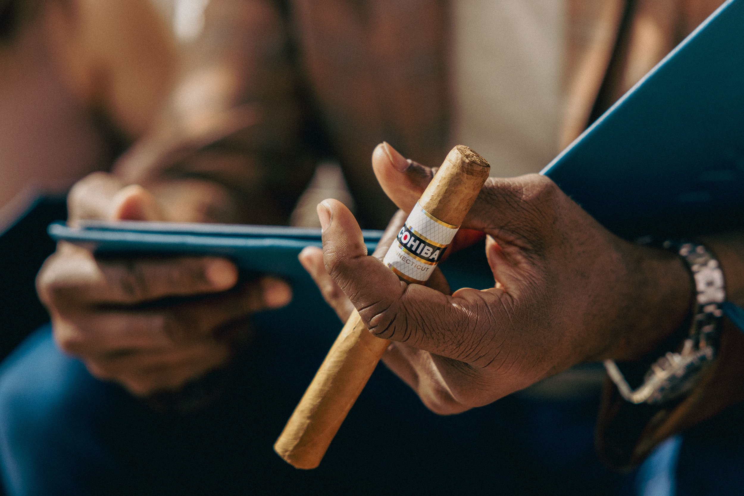 A person holding a cigar and a smartphone, with a blurred background.