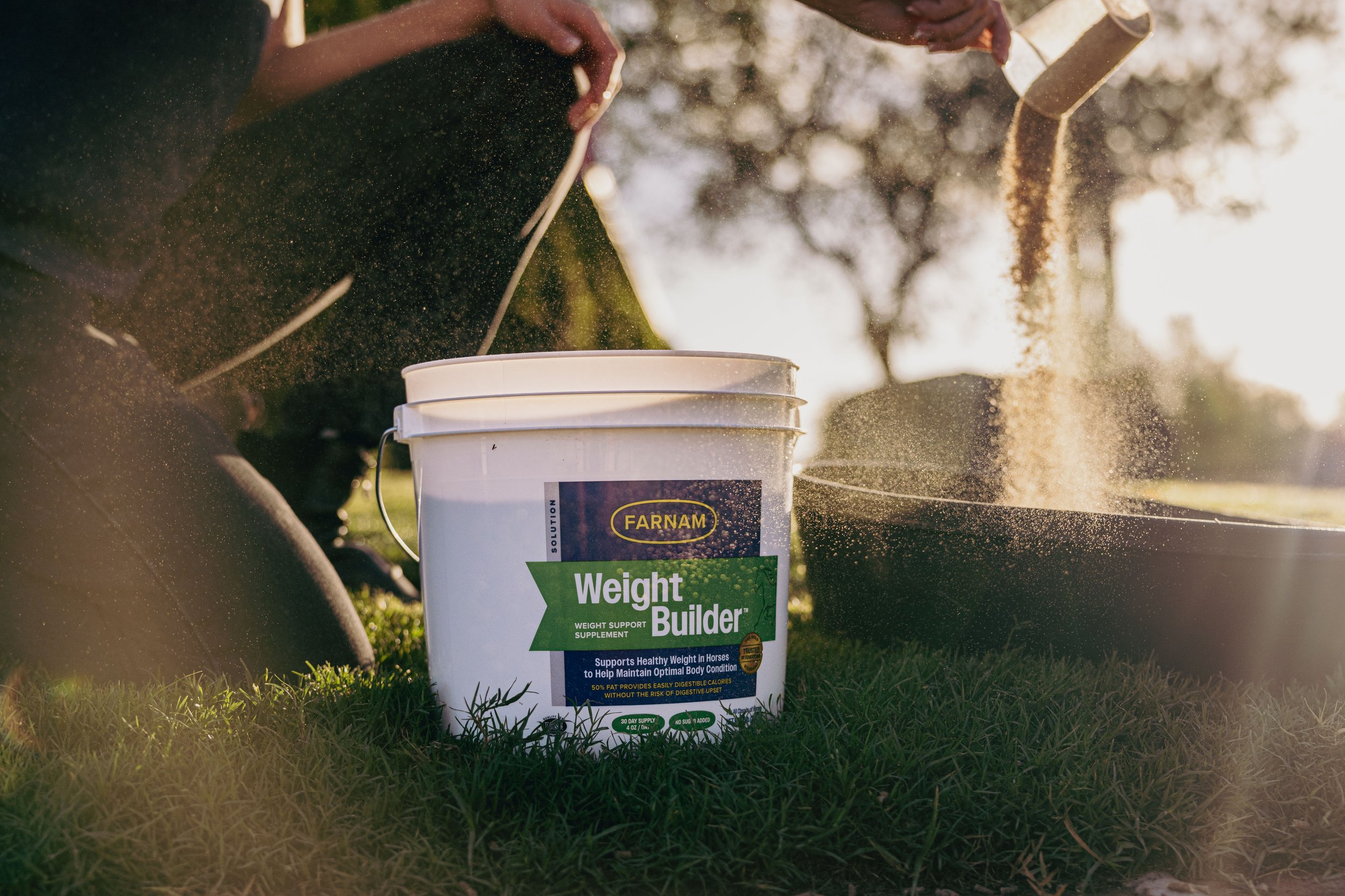 A person using a scoop to pour supplement into a container outdoors in sunlight.