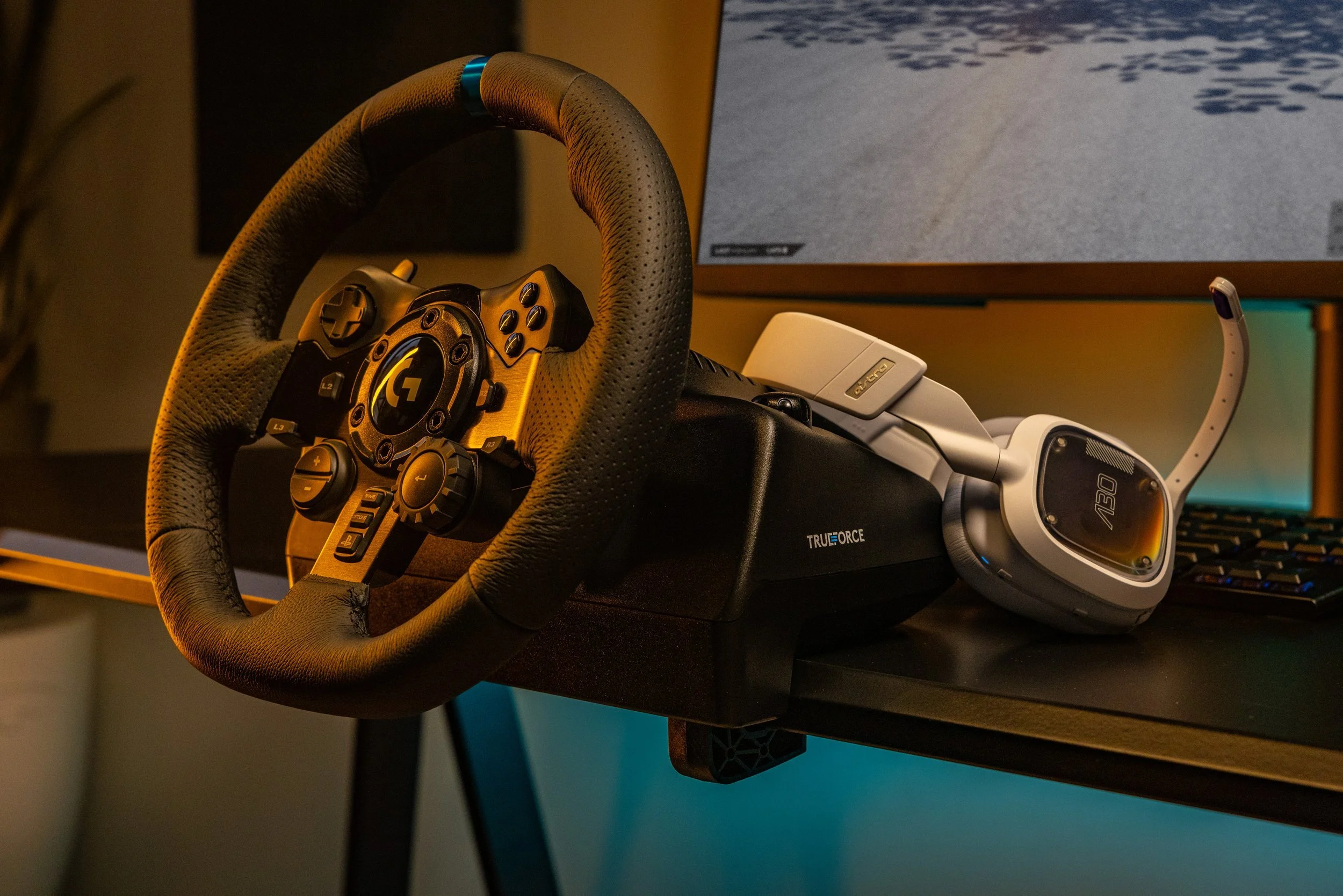 A racing simulator setup with a steering wheel, pedals, a monitor, and a racing headset on a desk.
