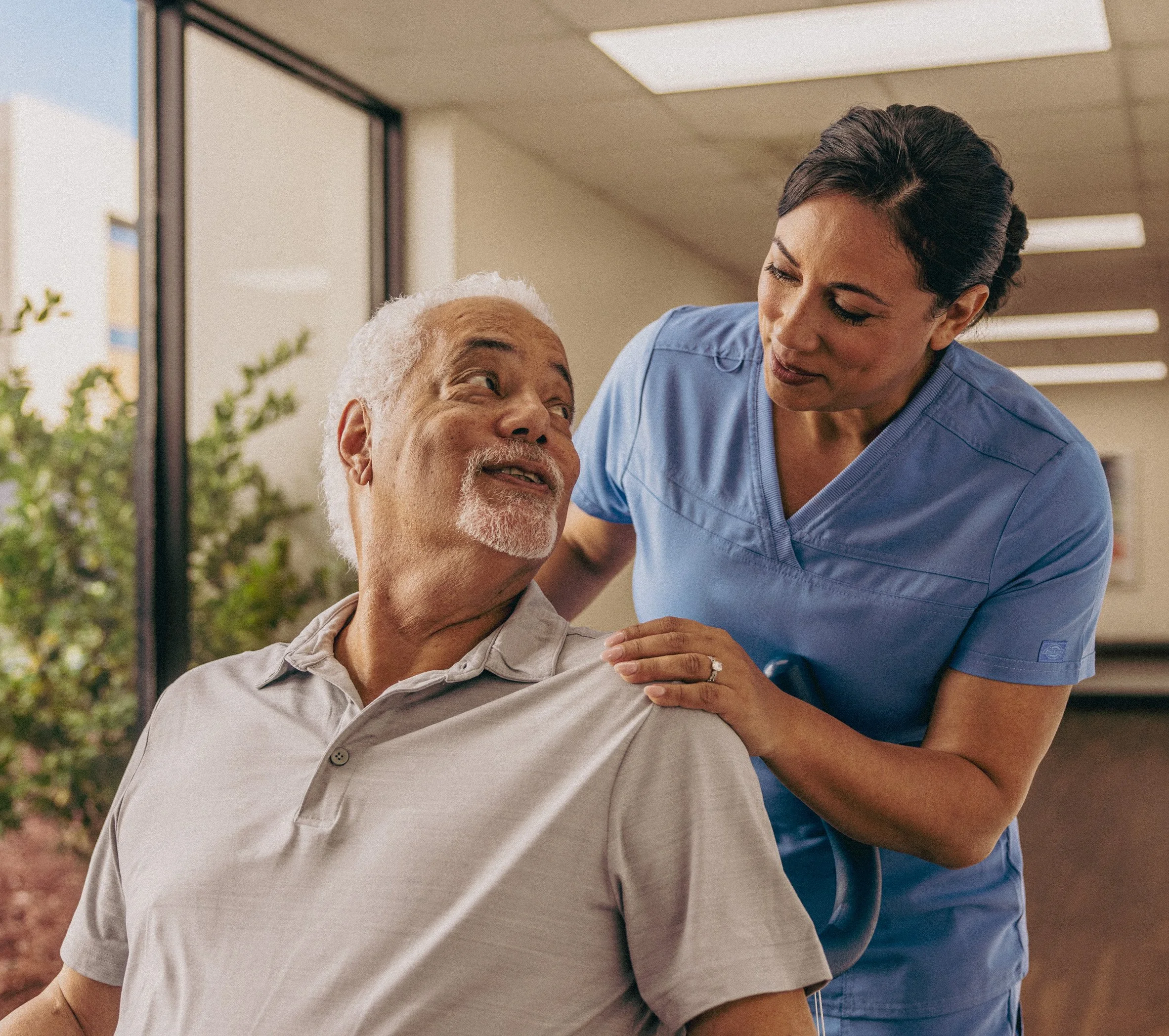 A healthcare worker, woman in blue scrubs, caring for an elderly man in a medical facility.