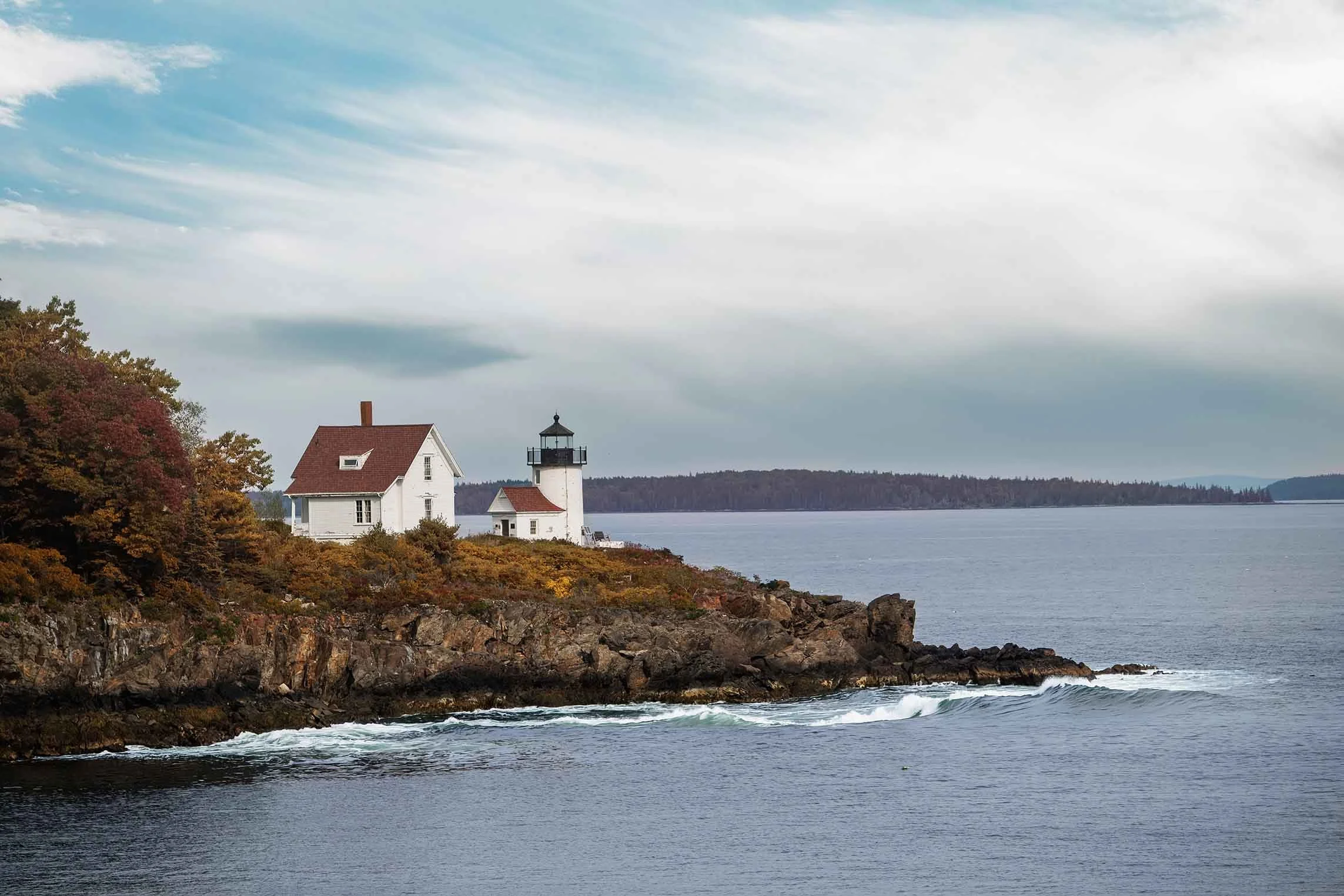 “Curtis Island Lighthouse in Camden, Maine captured in autumn, surrounded by warm fall foliage, rocky shoreline, and calm coastal water, photographed as fine art wall art for buyers seeking Maine lighthouse prints.