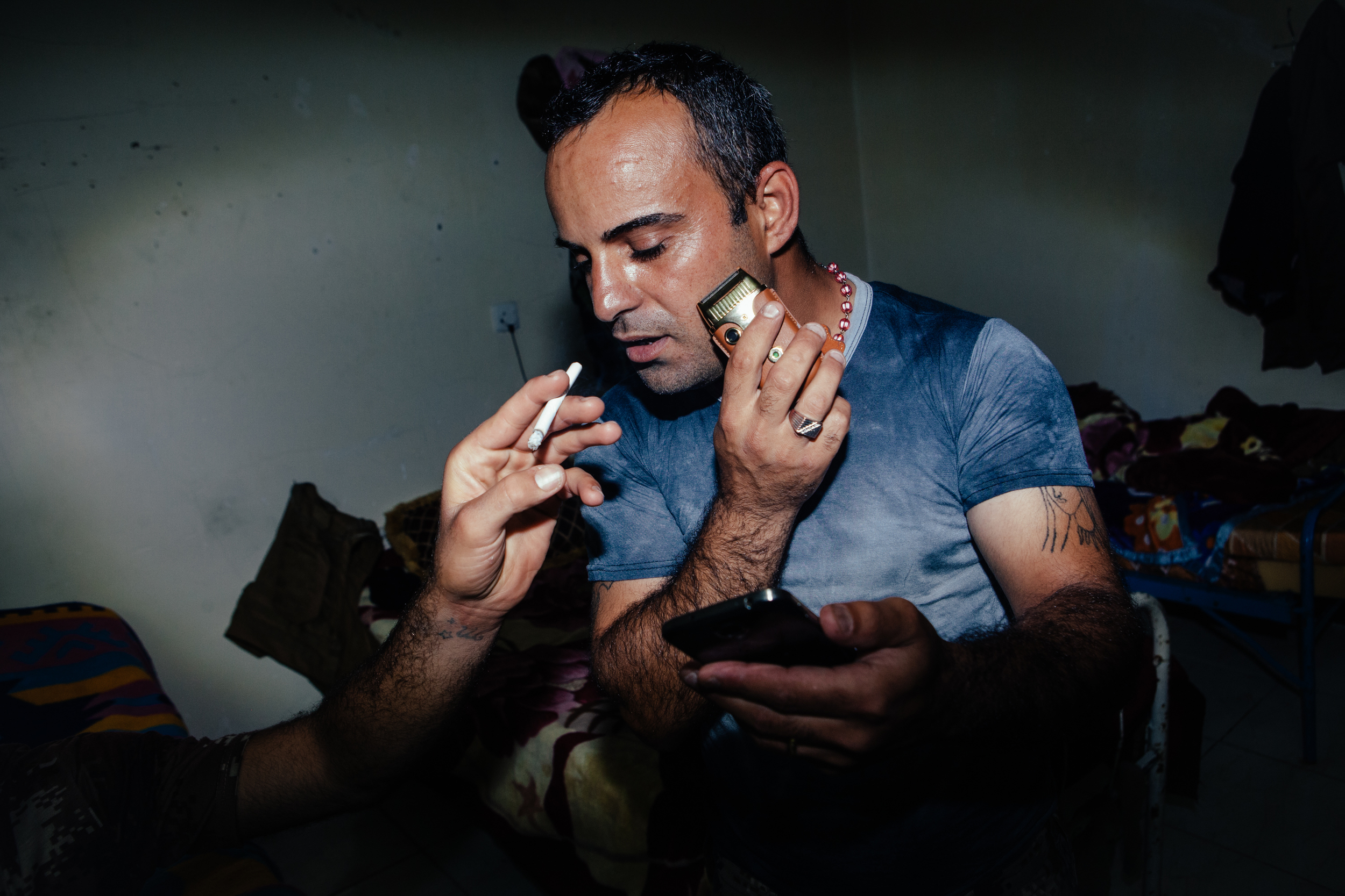  An NPU militia soldier shaves, looks at his phone and smokes a cigarette at an NPU military base near Sharafiyah, Northern Iraqi Kurdistan. 