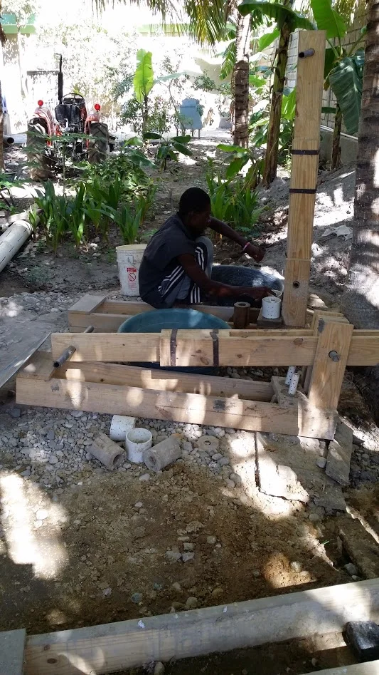 A briquette being created in the hand press. Briquettes are cheaper than propane, reduce deforestation and they clean up the environment by recycling waste. All of the school feeding in the 9 schools HT runs in Gonaives are prepared using briquette fuel.