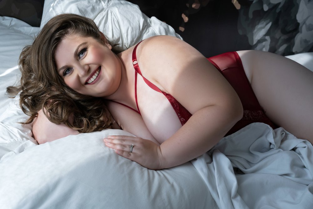 Plus size woman in red lingerie posing on a bed for a boudoir photo shoot at Demi Girl Photography in Chicago, IL.
