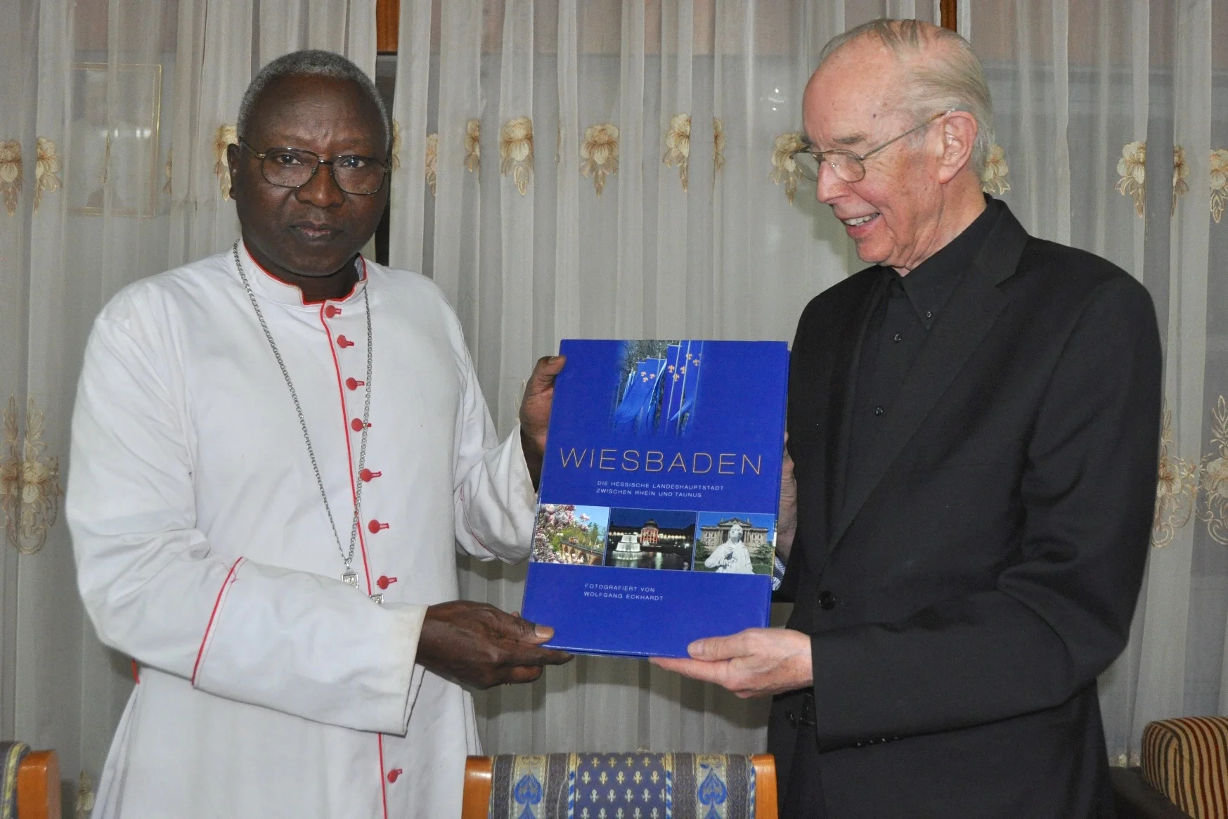 Das Foto zeigt Kardinal Philippe Ouedraogo mit Pfarrer Werner Bardenhewer im Januar 2016 in Burkina Faso bei der Überreichung eines „Wiesbaden-Bildbandes“.