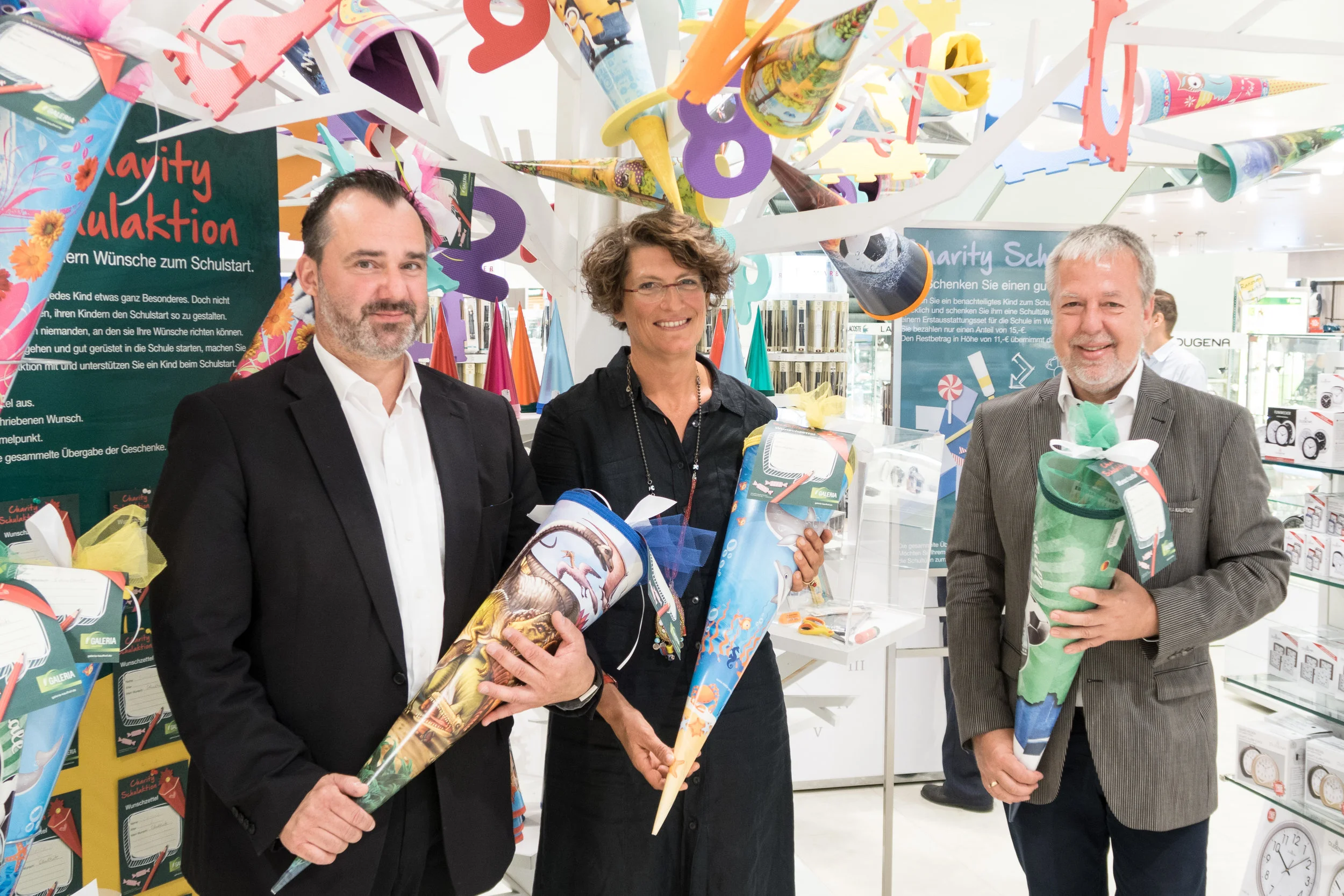 Abteilungsleiter Reiner Meyer (L), Kita-Koordinatorin Dr. Julia Fauth (M) und Filialleiter Karsten Sinnig (R) vor dem "Schultüten-Baum" im EG der Wiesbadener Galeria Kaufhof Filiale.