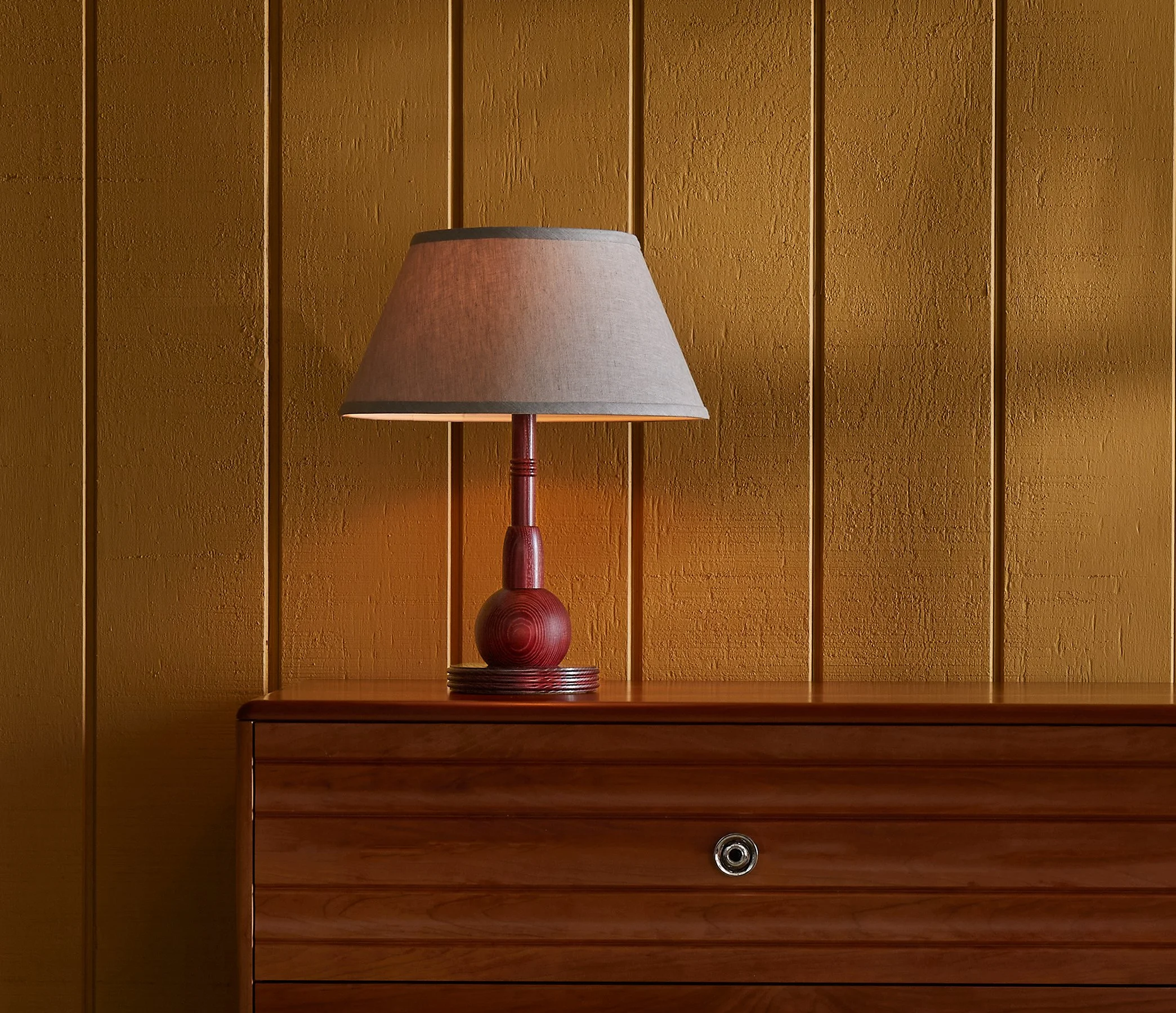 The Neria Lamp is a made-to-order accent table lamp from O&G Studio, crafted in solid hardwood shown here in Oxblood stain on ash atop and O&G Edda Dresser in cherry