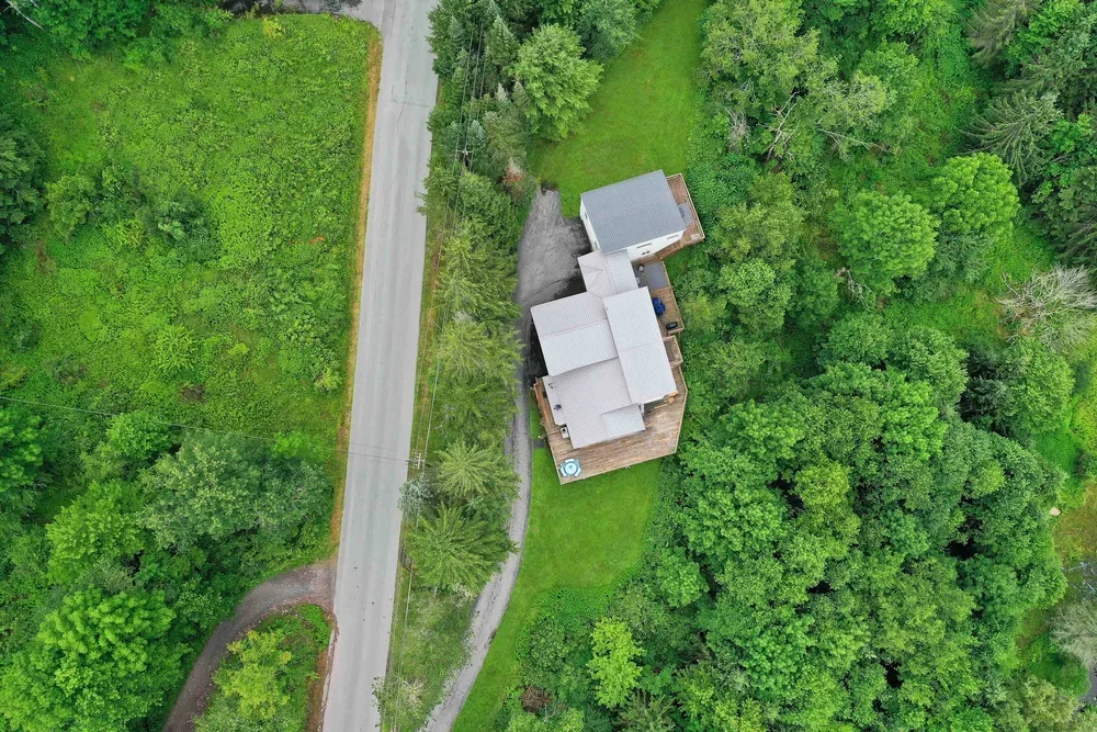 Aerial view of a house surrounded by trees and greenery, with a road nearby.