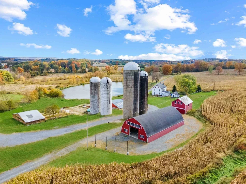 A farm scene with a red barn, silos, a pond, and surrounding fields in autumn.