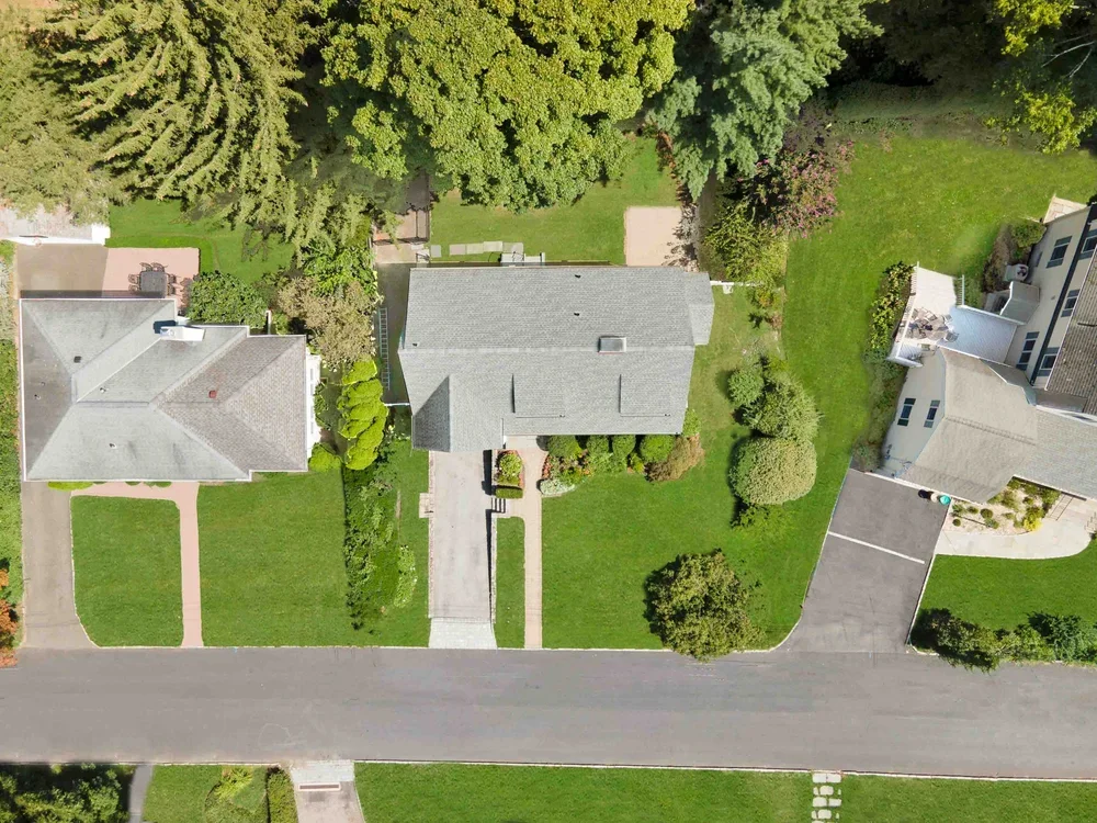 Aerial view of residential neighborhood with three houses, green lawns, trees, and driveways.