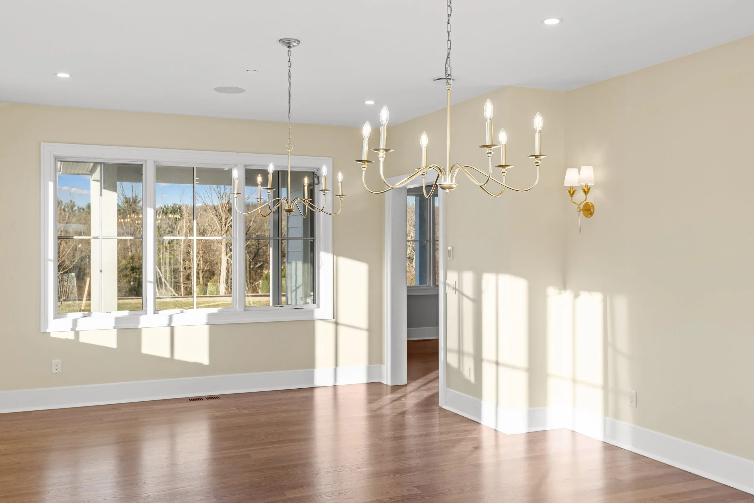 Empty dining room with large window, chandelier, walls painted light beige, and hardwood flooring.