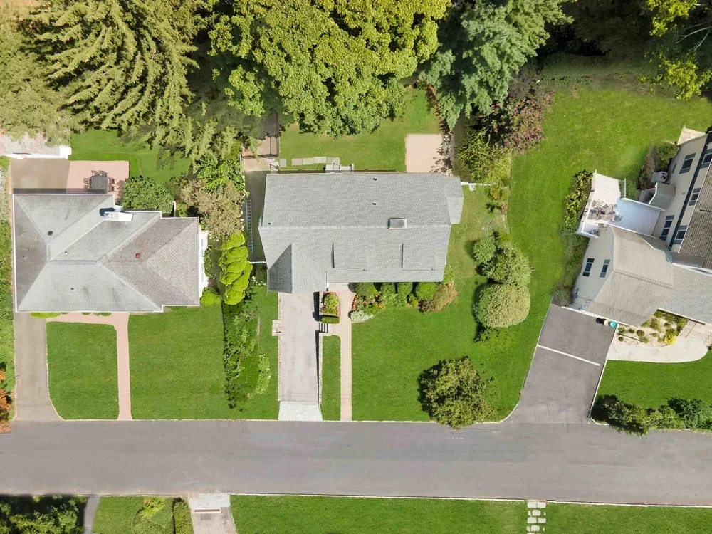 Aerial view of three houses with green lawns, trees, and a street in front.