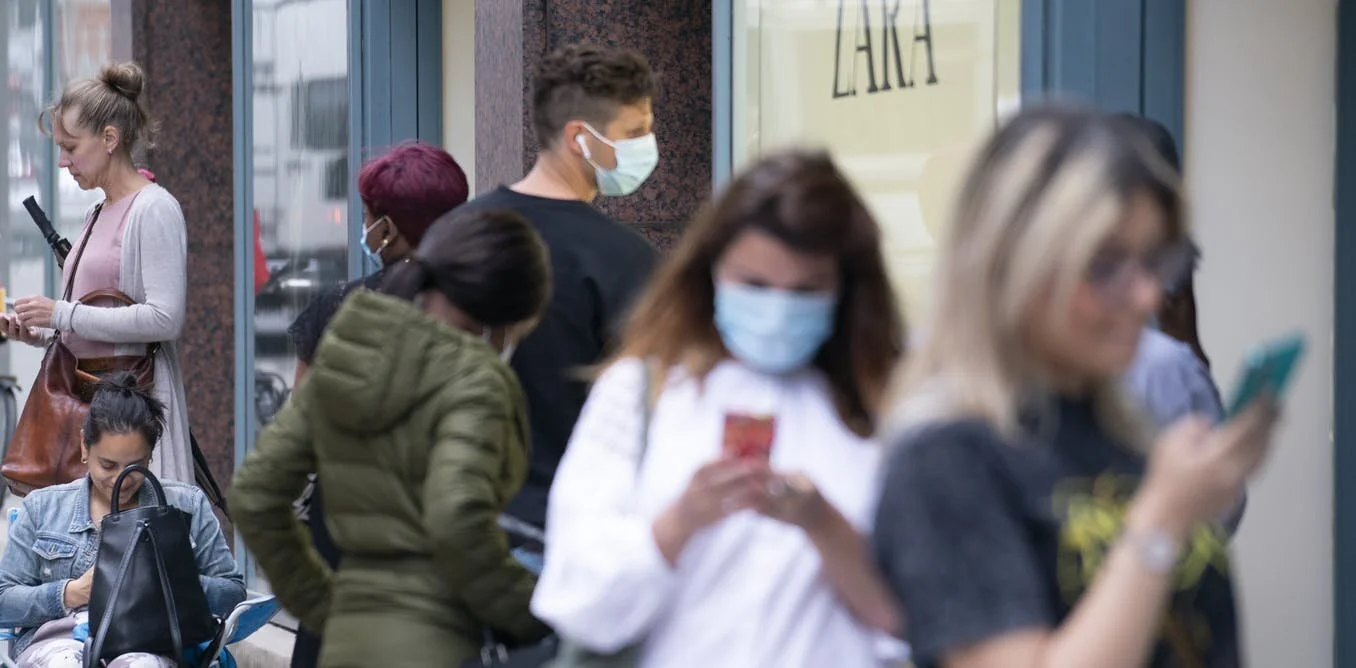 group of shoppers wearing masks and looking at their phones outside zara store