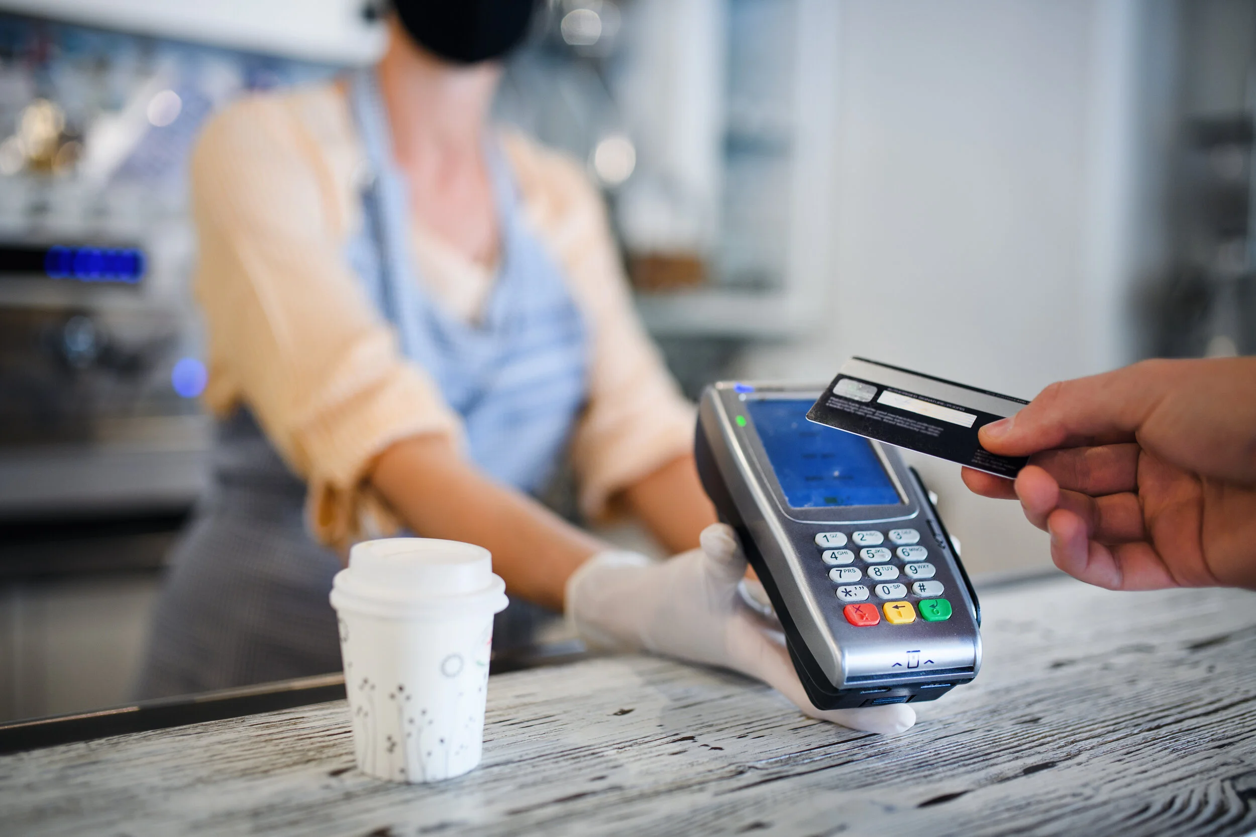 customer pays for coffee using contactless payment while cashier wears gloves and mask