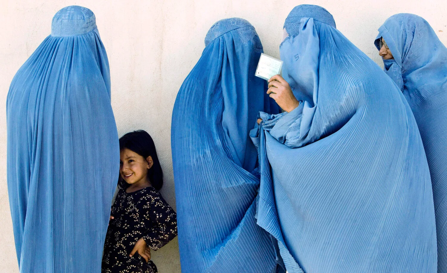 Group of women wearing blue burqas with a smiling child standing nearby.