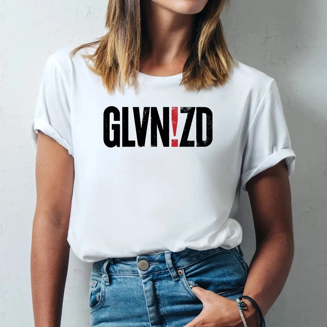 Branded T-shirt merchandise in black and red compressed block letters worn by a girl with shoulder-length blonde hair. Her head is cropped at the chin and the shirt is tucked into traditional denim jeans.