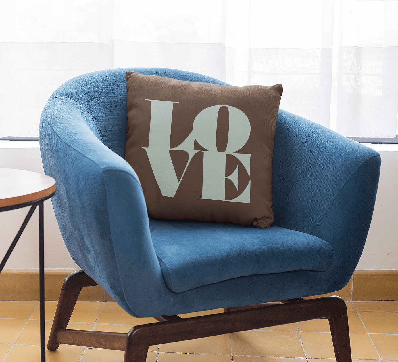 Blue upholstered armchair with a decorative pillow that says 'LOVE' in large letters, placed near a window with sheer curtains in a cozy room.