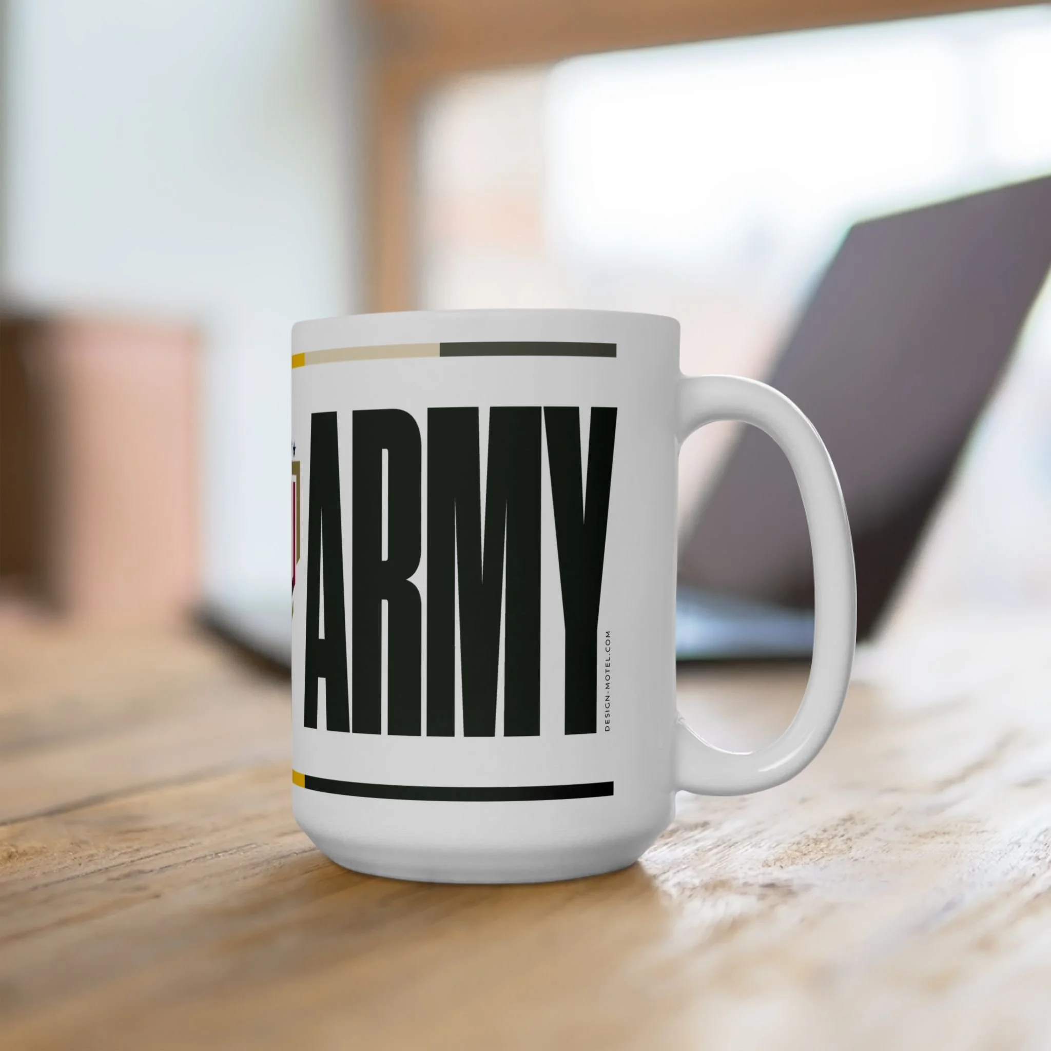 White coffee mug with Army-themed text on a wooden table, with a blurred laptop in the background.
