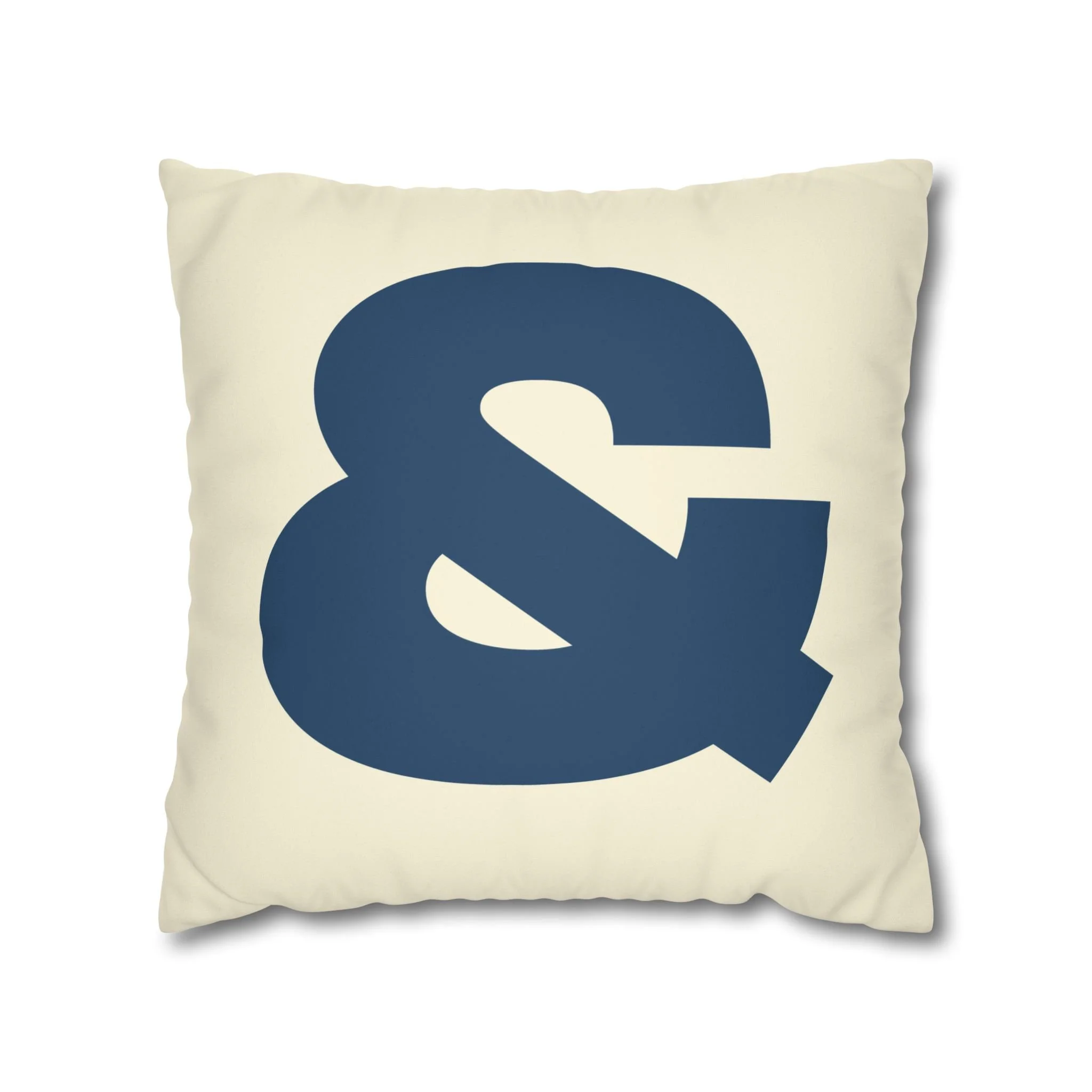 A beige decorative pillow with a large navy ampersand symbol.