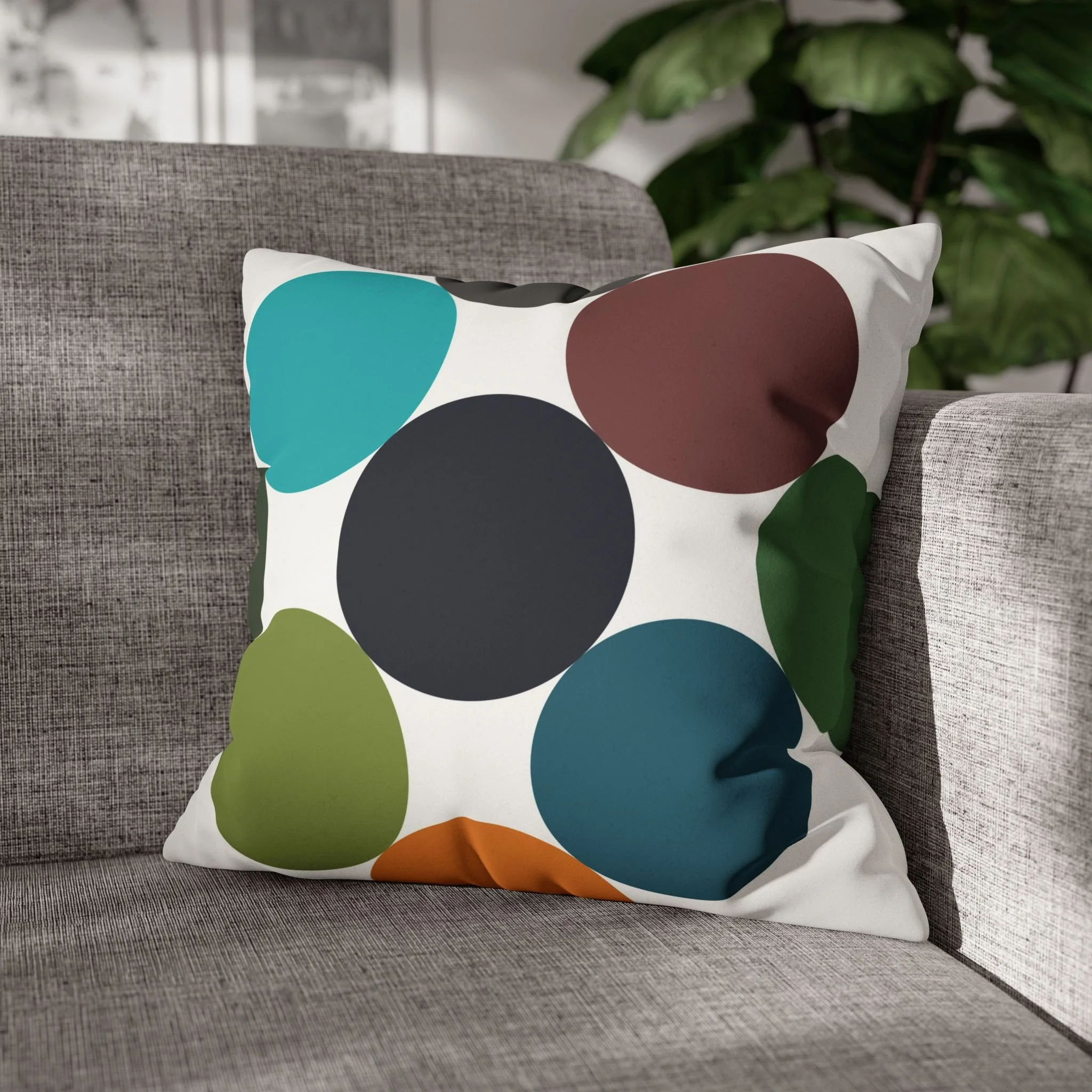 Decorative pillow with polka dot pattern in blue, green, brown, and black on a gray sofa, with a green plant in the background.