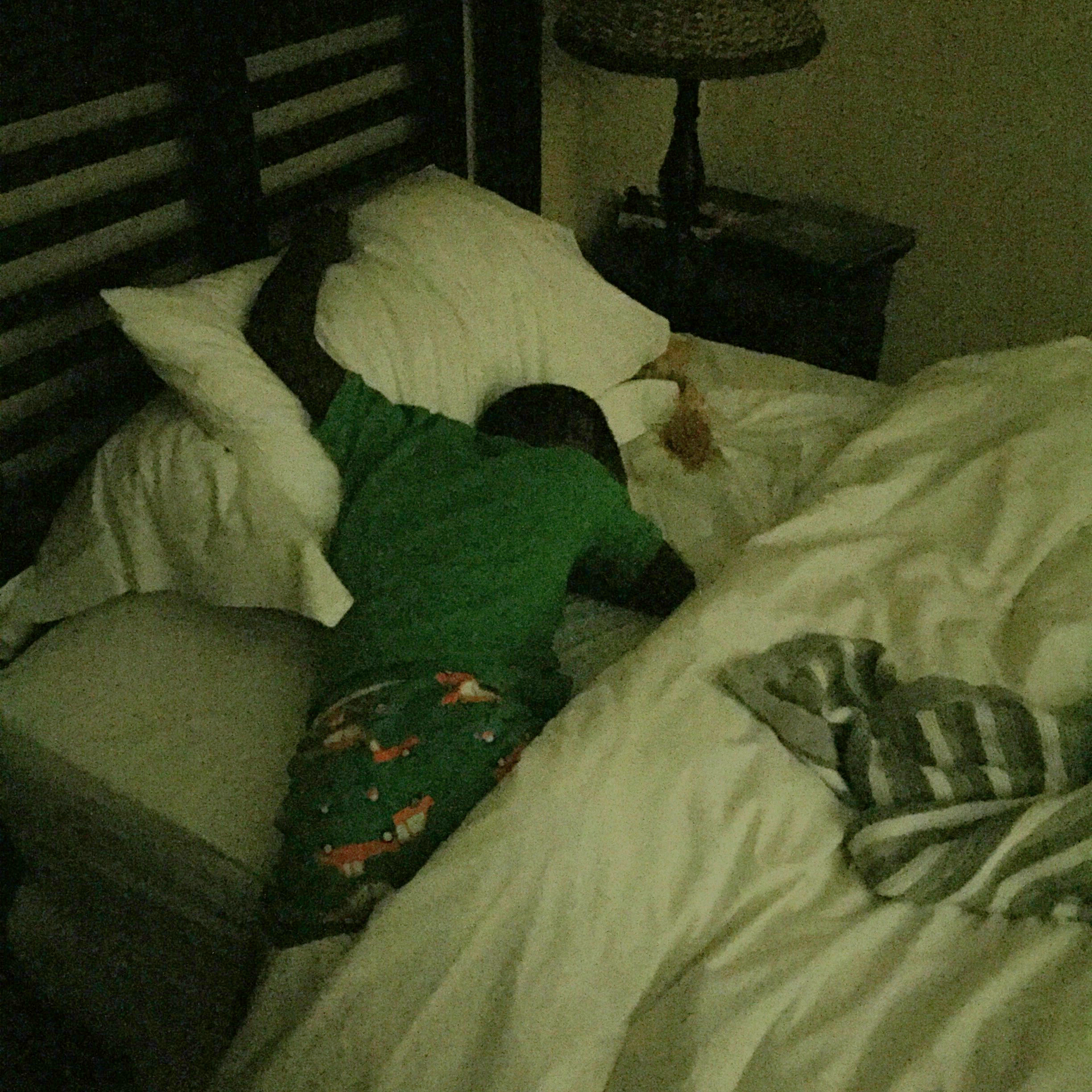 Laying across the bed with his legs off the side, while holding onto his pillow for safety.