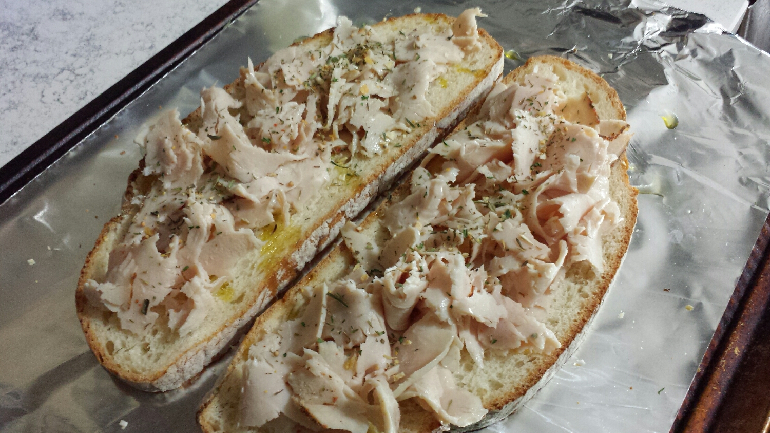First, line a baking sheet with foil and place two pieces of bread on top, drizzling with olive oil. Next take any left over meat (your favorite deli meat, or last night's dinner), shred it, and place it on top of the bread. We used roasted turkey deli meat. Sprinkle with 1 tsp of South of France and place on the top rack of the oven at 400°.