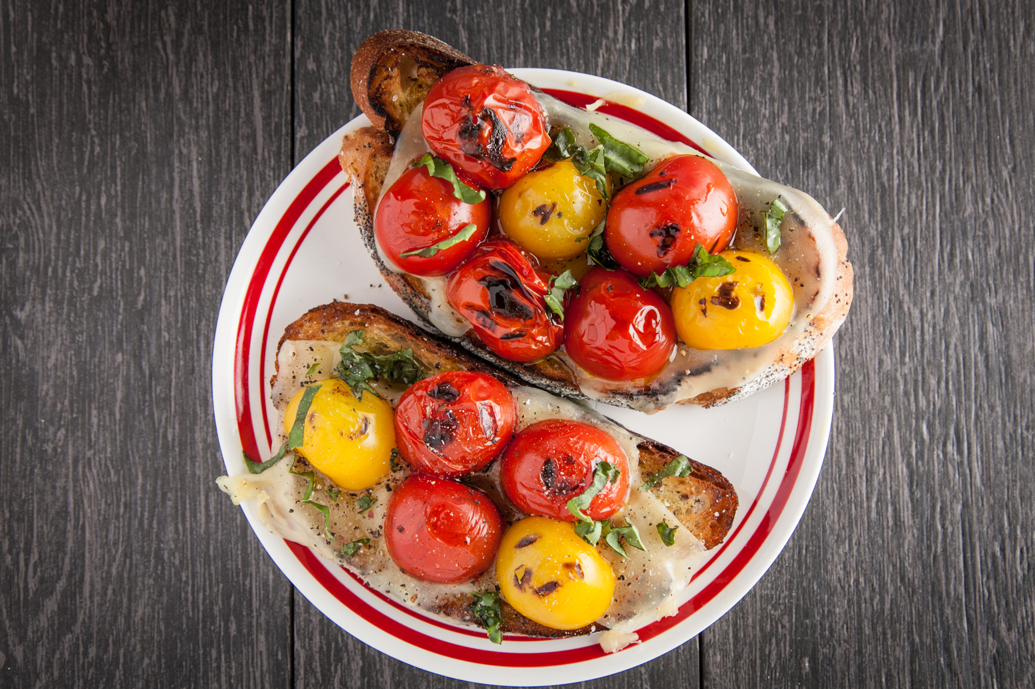 Roasted cherry tomatoes on grilled french bread, with a dab of spicy hot oil and a few shavings of basil
