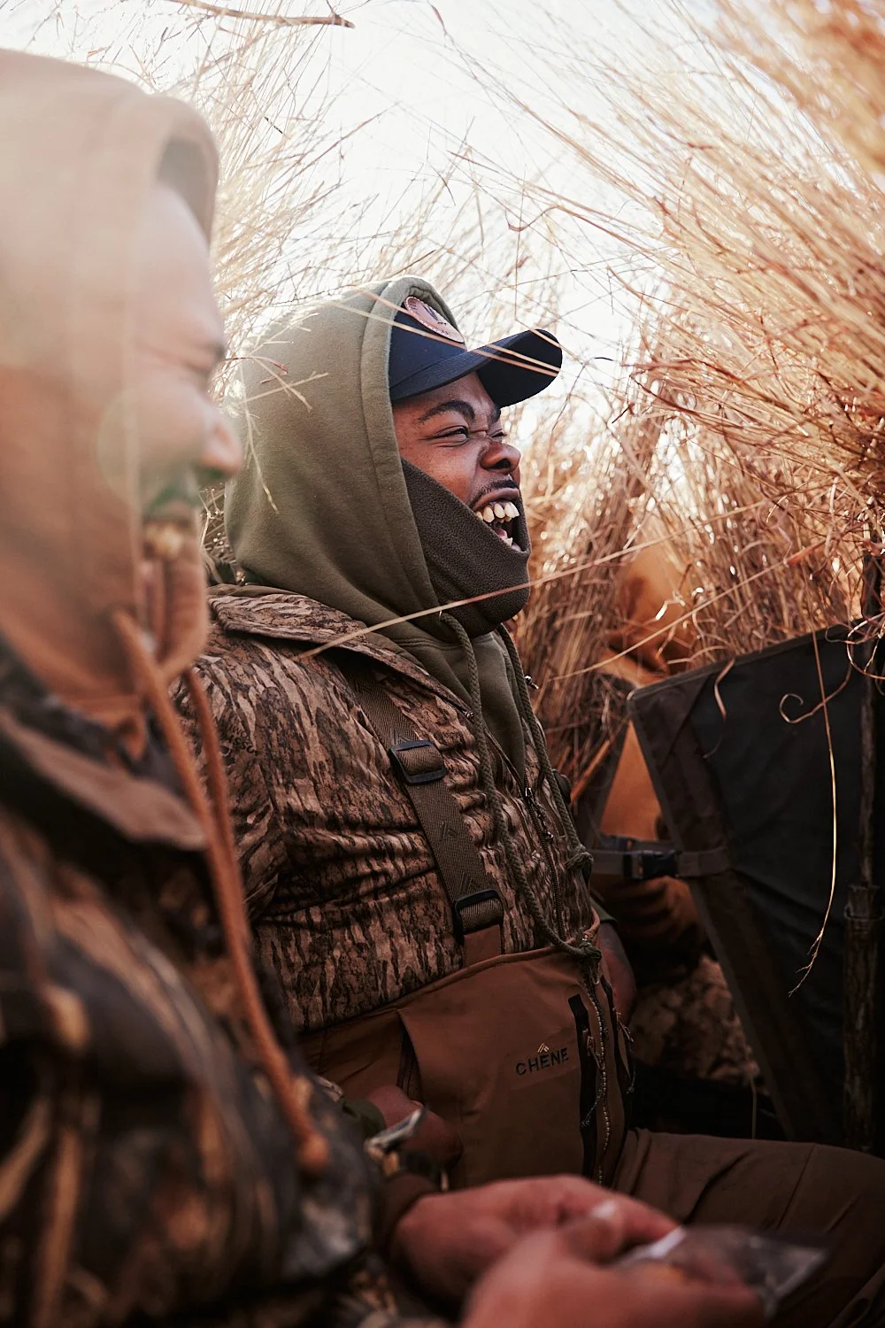 Lifestyle commercial duck hunting photo of 2 hunters wearing camo laughing in a duck blind during a duck hunt in Kansas shot by photographer Ian Mahathey.