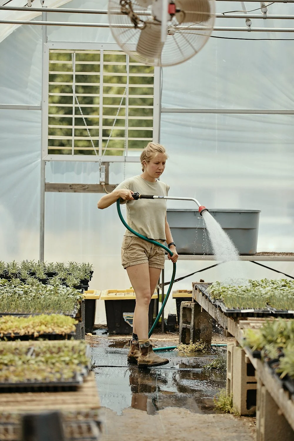 A woman in a greenhouse waters plants at a vegetable garden on a farm in North Carolina, shot by photographer Ian Mahathey.