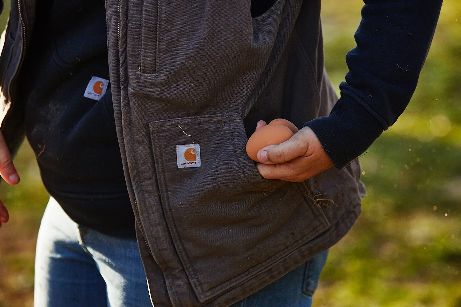 Lifestyle commercial photograph of a woman wearing a Carhartt vest and holding chicken eggs on a farm in South Carolina, shot by photographer Ian Mahathey.