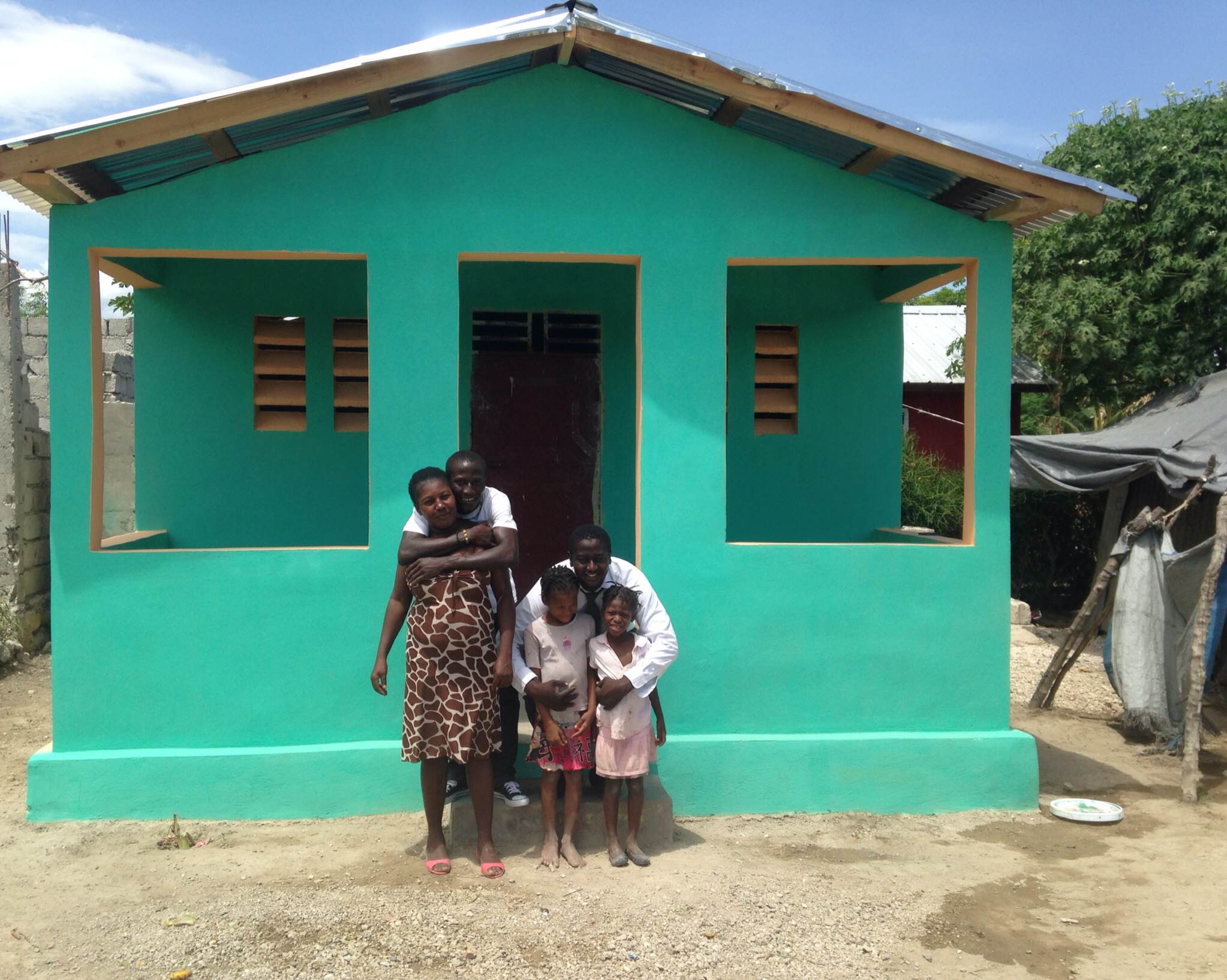 Maculla and her family with our In-Country Director, Jimmy, standing in front of their new home.