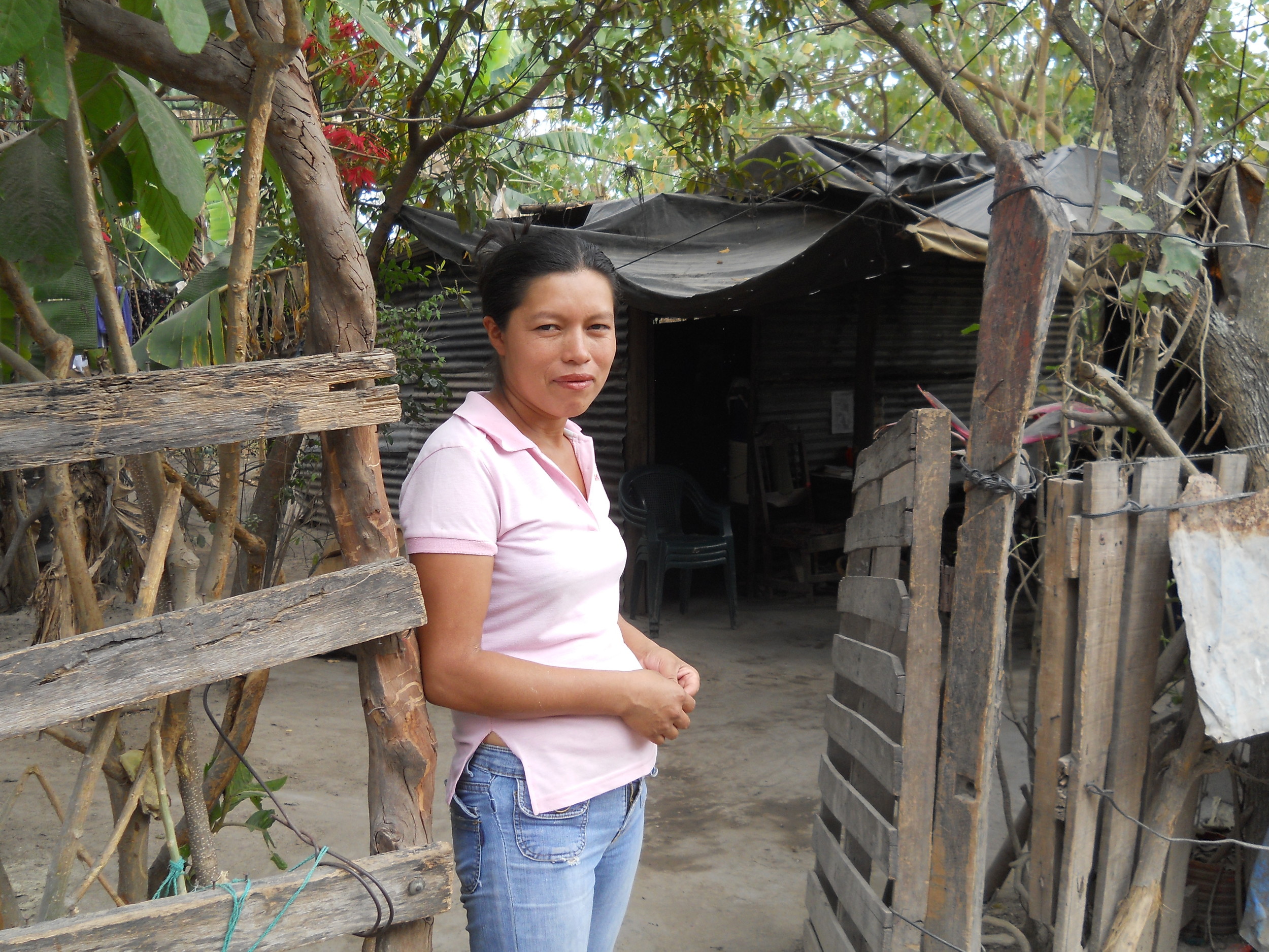 A woman in The Romero Community stands in front of the shack where she lives.