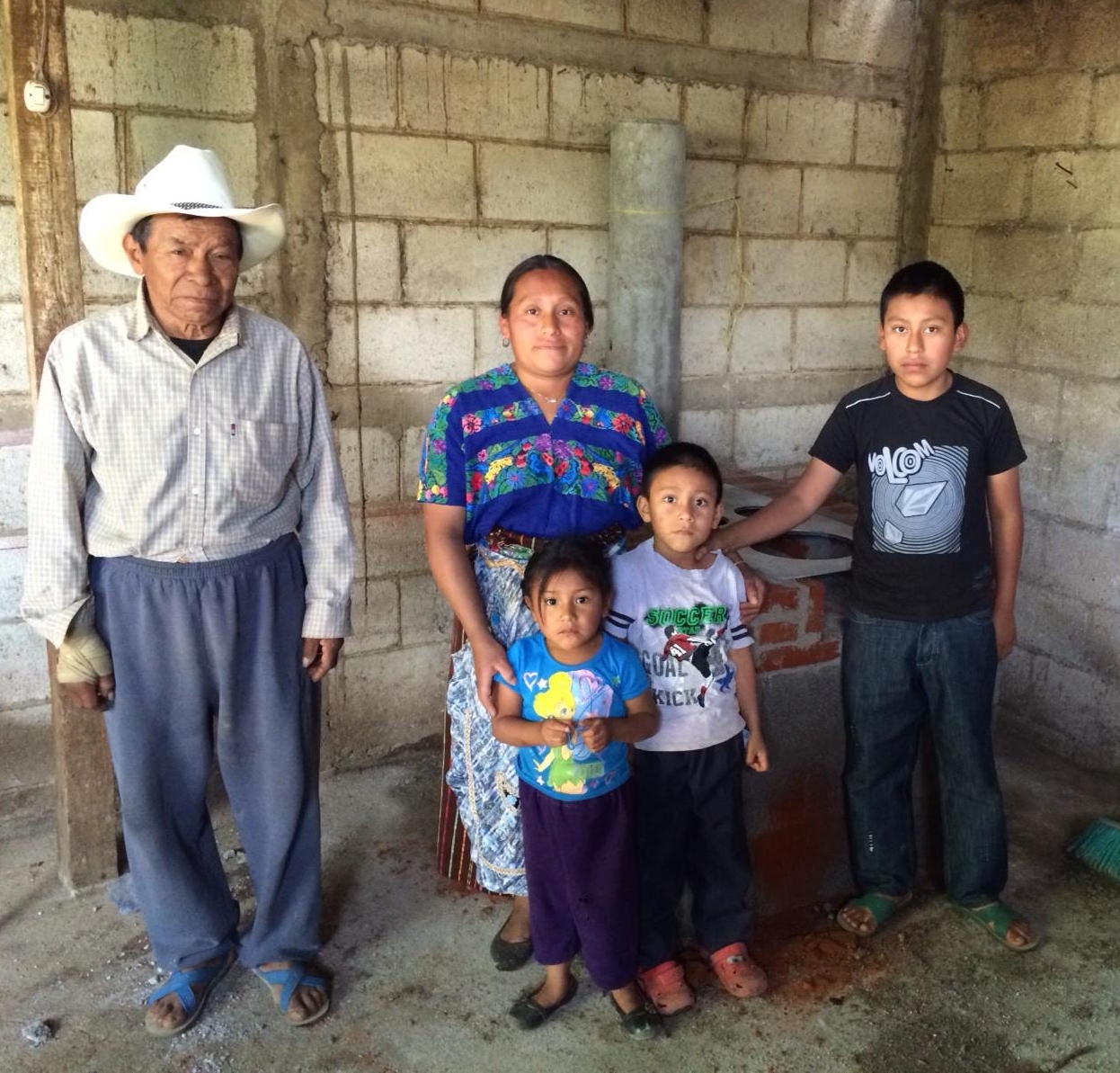 A Guatemalan family stands inside their new home in front of their new stove, both built by a team of Homes from the Heart volunteers.
