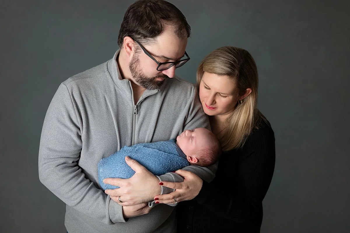 Chesterfield Virginia Newborn Photographer, Parents holding and looking down at their newborn baby wrapped in blue during a photo session in Chesterfield VA close to Mechanicsville