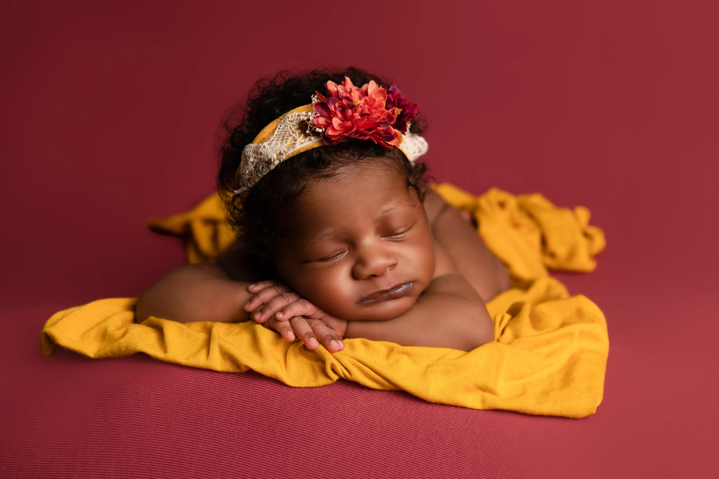 newborn baby girl posed on a golden yellow wrap with a mauve blanket and autumn colored floral headband in Richmond Virginia