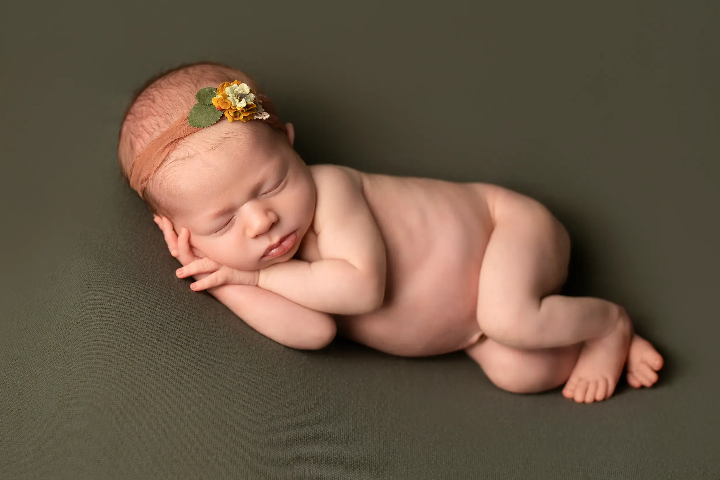 Sleeping newborn baby on a forest green blanket with a natural flower headband for newborn portrait in Chesterfield Virginia