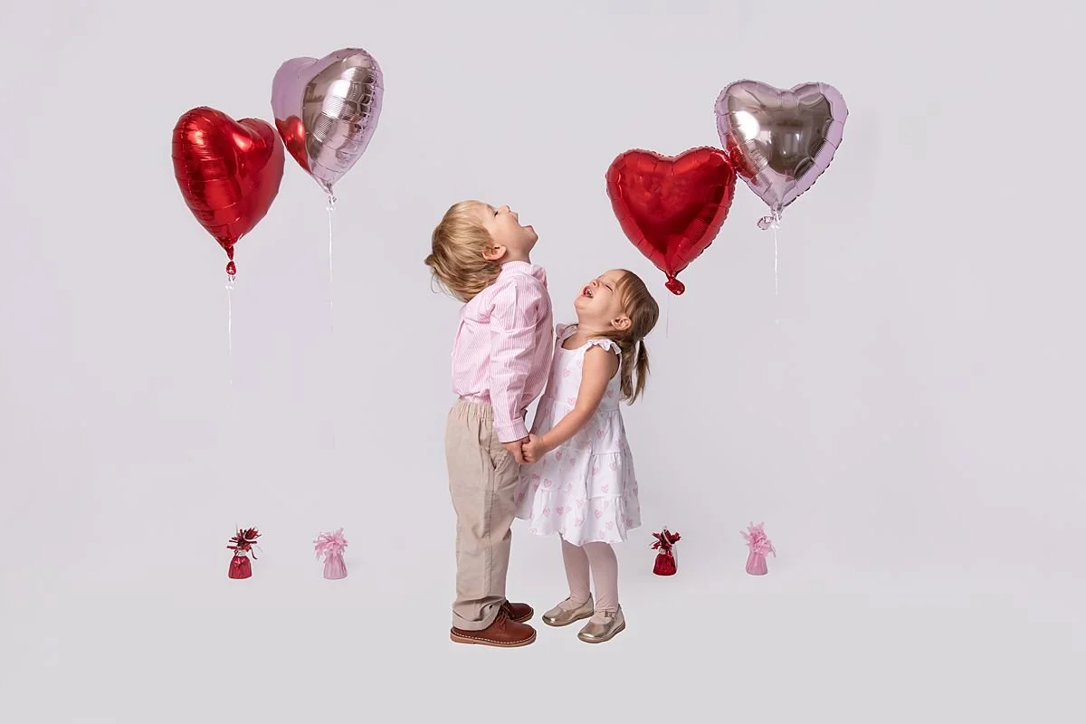 Brother and sister holding hands laughing with red and pink balloons photographed by Sarah Kane Photography near Richmond VA