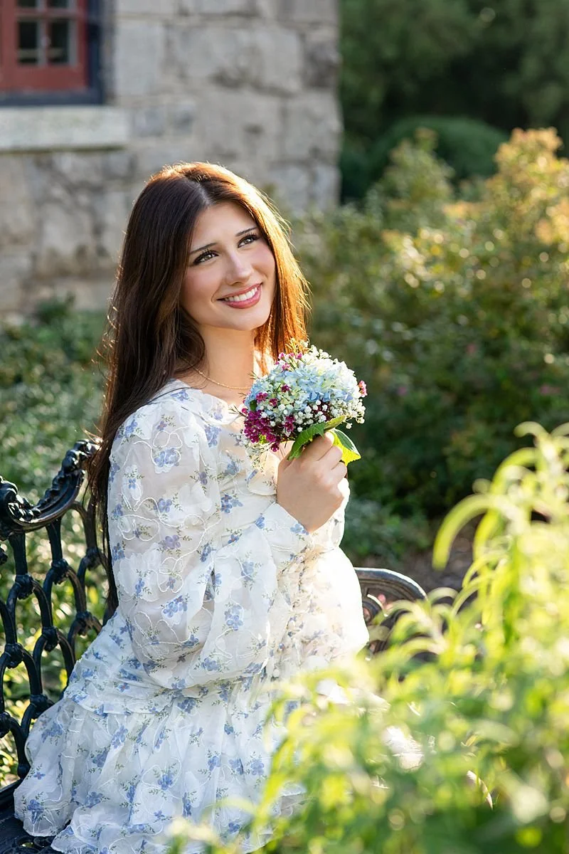 Photos of a High School Senior Female in a white and blue floral dress holding a bouquet for senior portraits at Maymont Park in Richmond Virginia