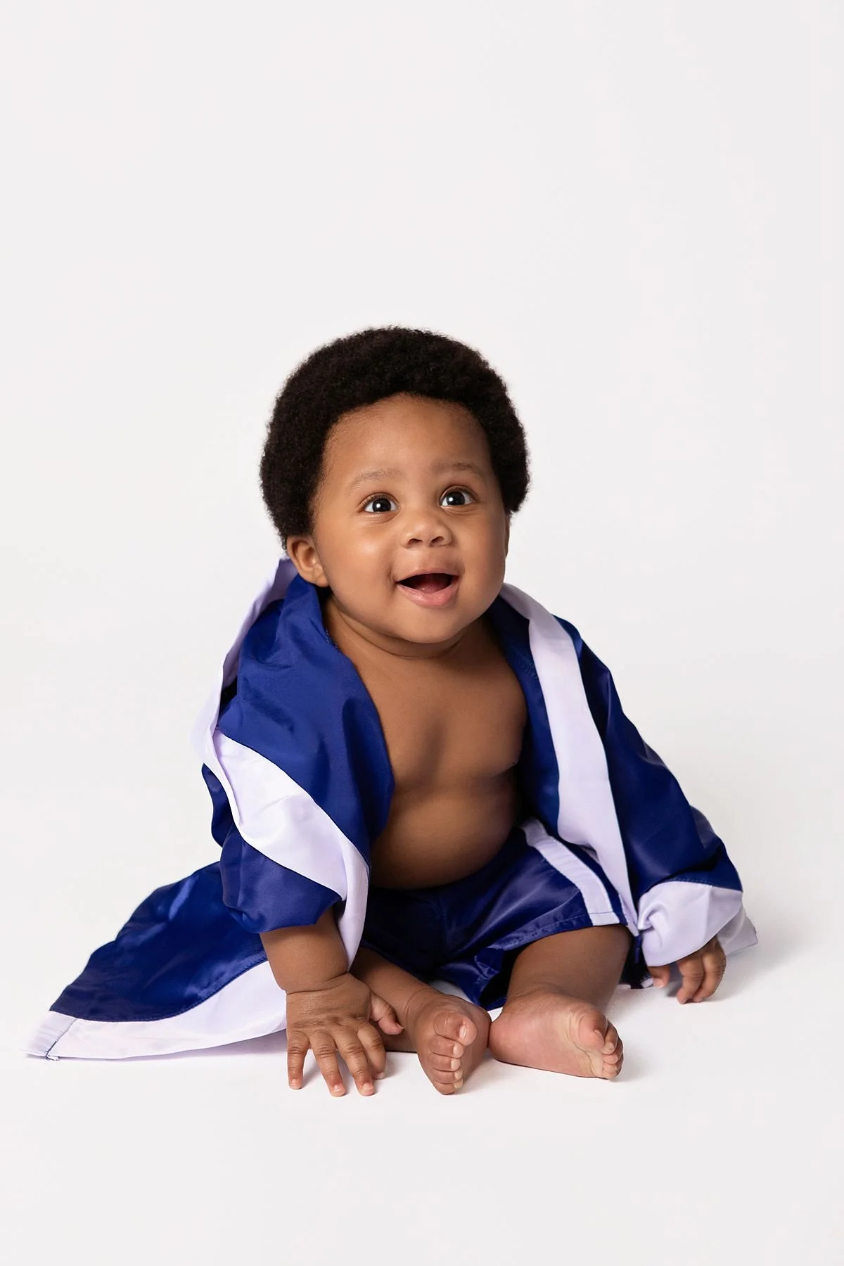 Smiling baby boy wrapped in a blue satin boxing robe during his half birthday session by Sarah Kane Photography, Chesterfield VA