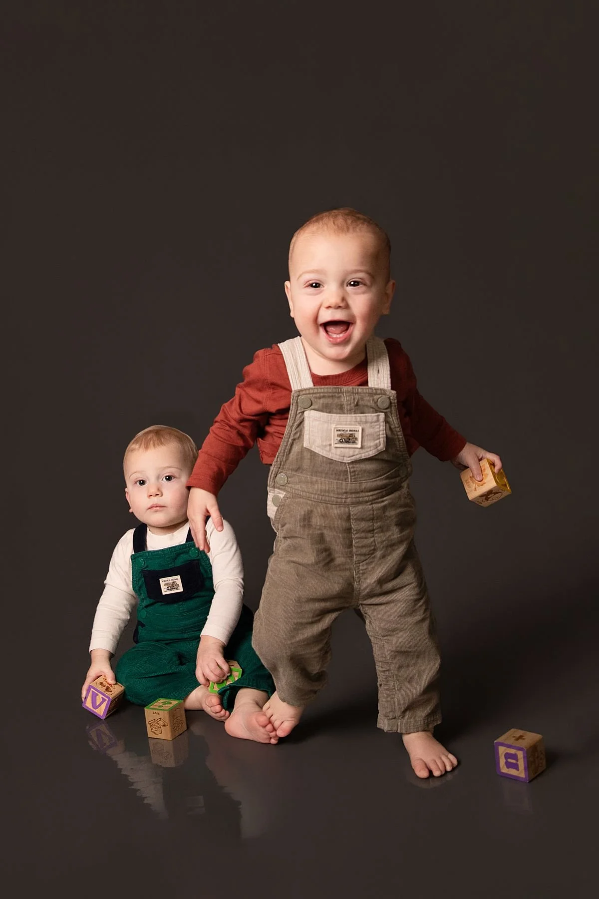 Twin one year olds playing with blocks with one sitting and one standing by Sarah Kane Photography