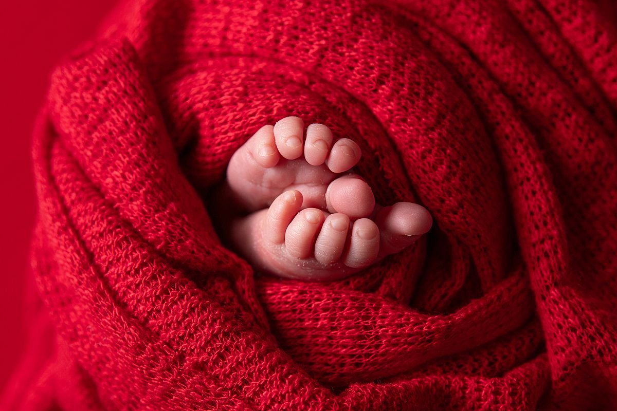 Close up of newborn baby toes peeking from red knit swaddle, Sarah Kane Photography
