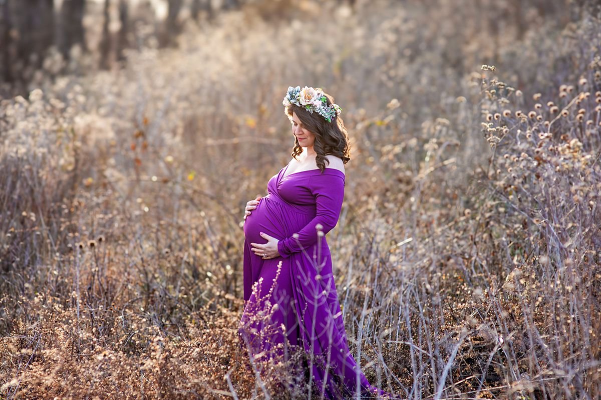 Pregnant woman in a purple gown and floral crown gazing down at her bump in a field at The Carillon, Richmond VA, Sarah Kane Photography