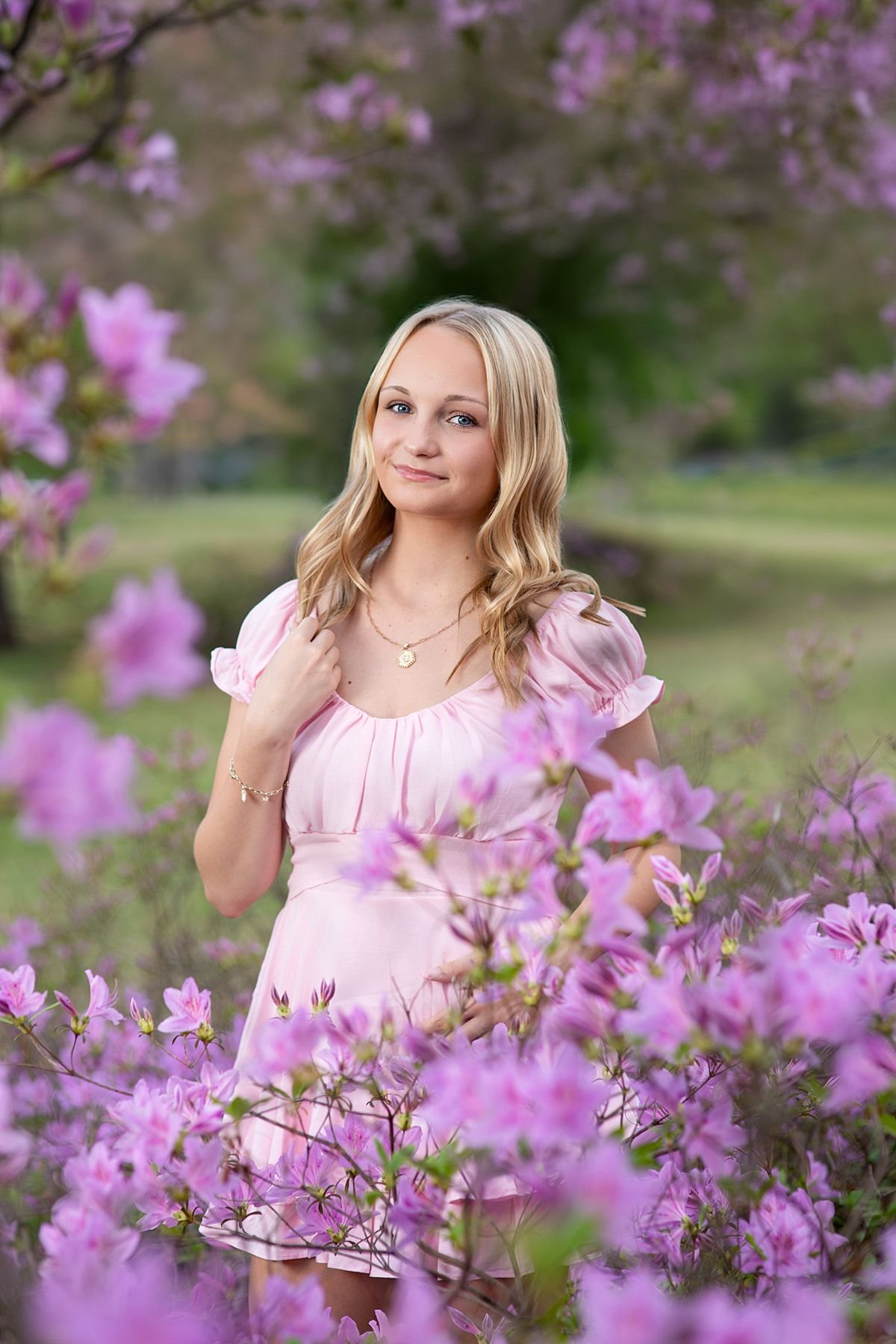 Close up spring senior portrait of a blonde teenage girl in a pink dress surrounded by purple flowering bushes, photographed by Sarah Kane Photography in Chesterfield, Virginia near Richmond