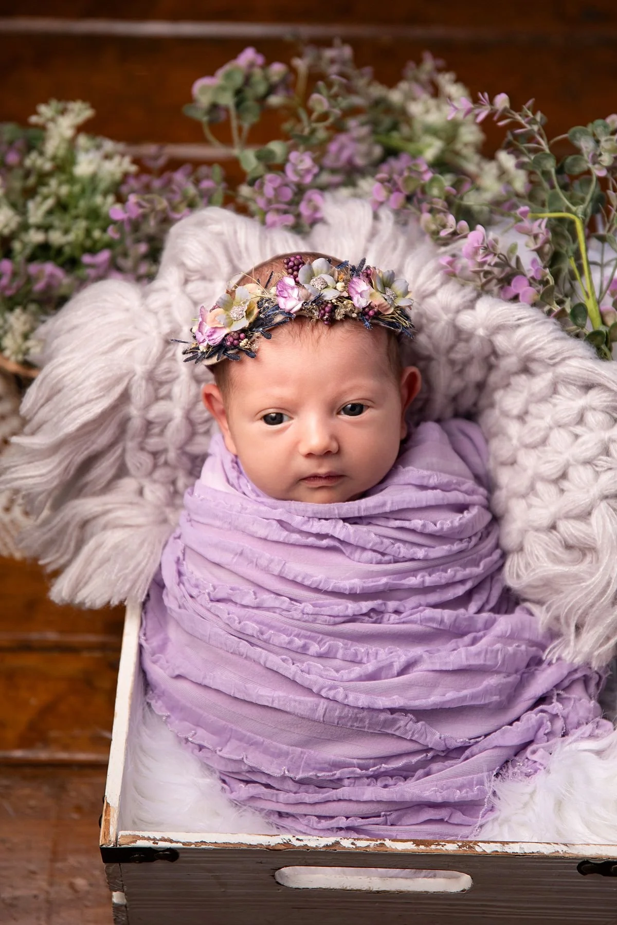 Newborn girl in lavender wrap and floral crown in white crate with purple florals, Sarah Kane Photography
