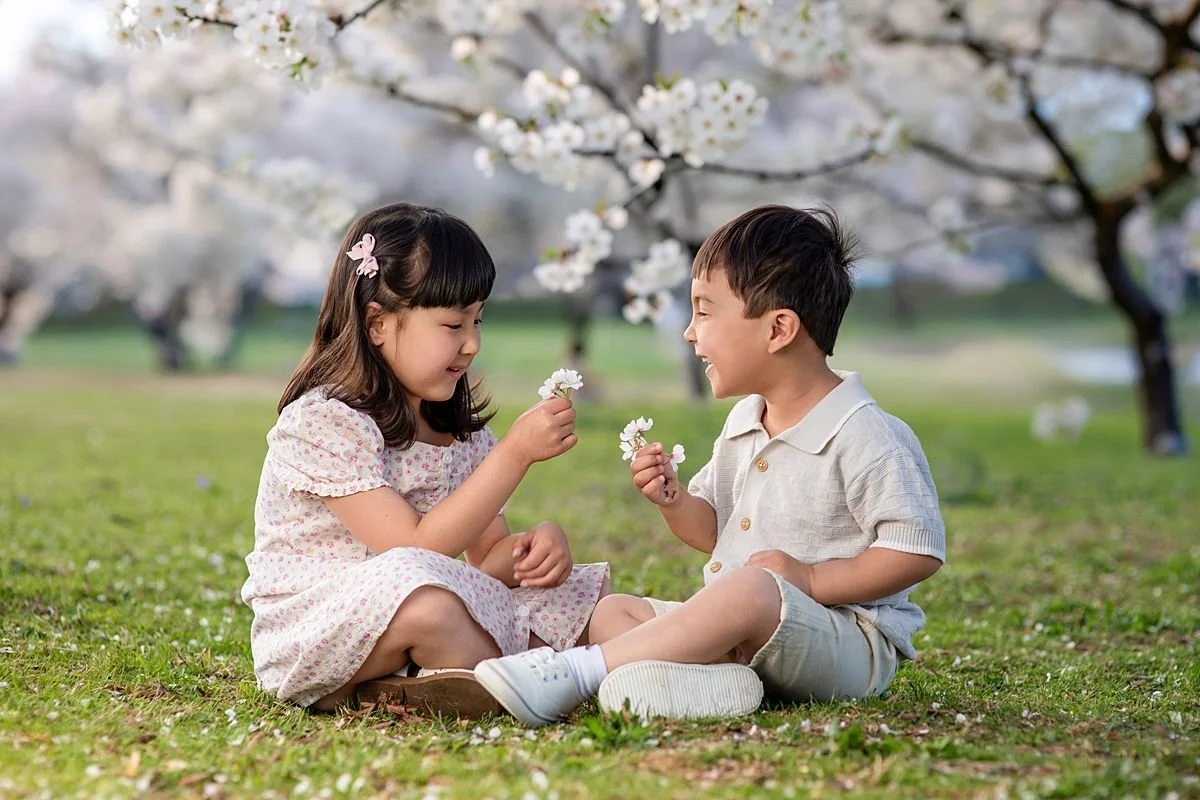 Brother and Sister sitting together holding cherry blossoms under trees, Sarah Kane Photography, Richmond Virginia
