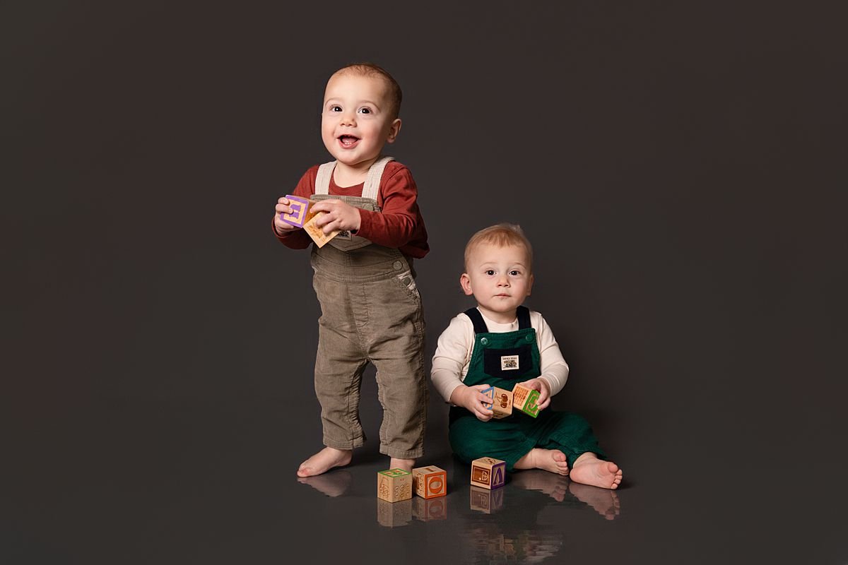 Twin one year olds standing and sitting with blocks by Sarah Kane Photography
