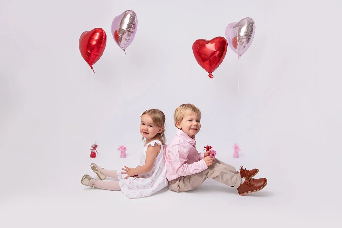 Brother and sister sitting back to back with valentines balloons photographed by Sarah Kane Photography near Richmond VA